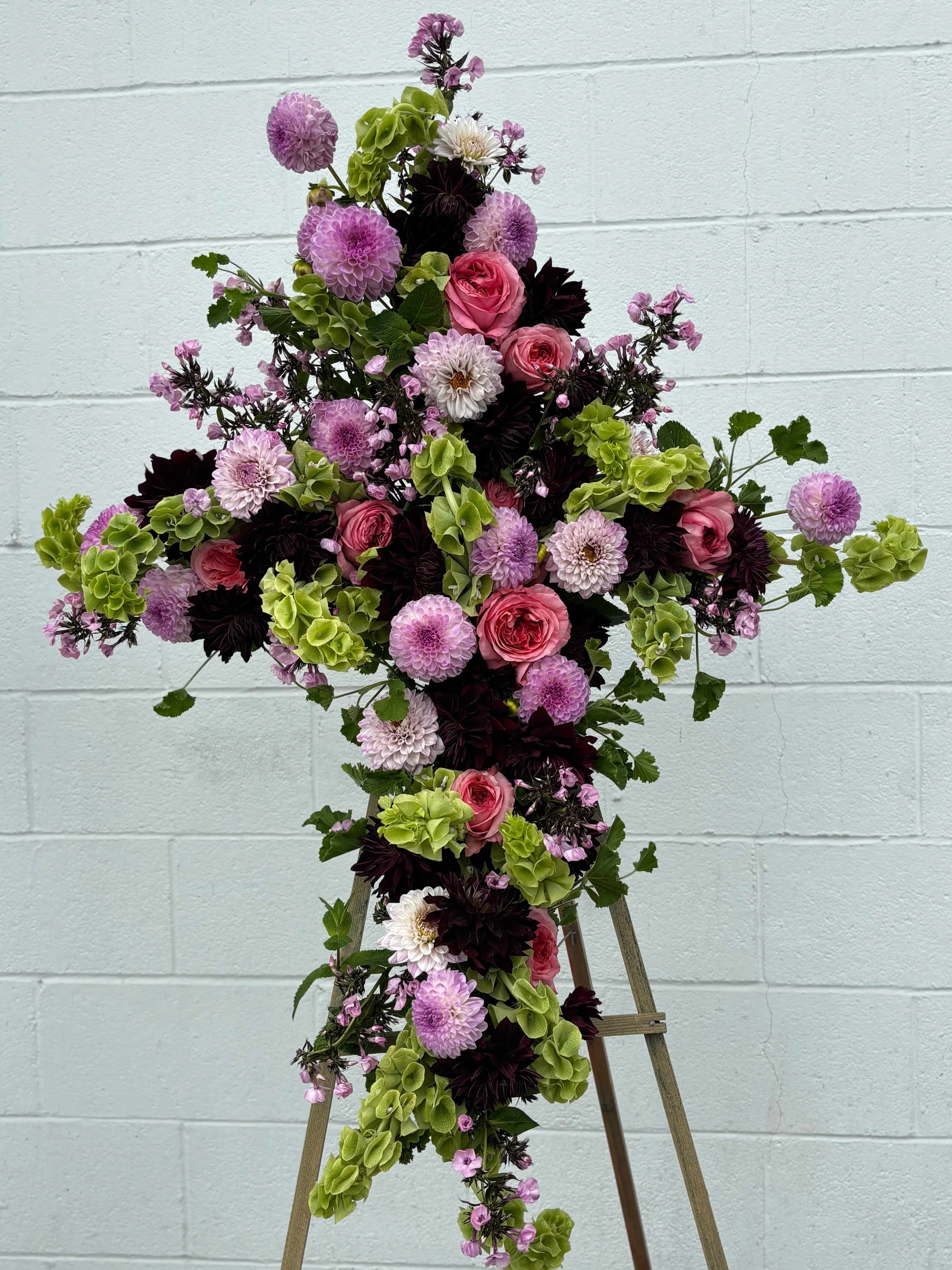 Cross-shaped floral arrangement with pink, purple, white, and green blooms