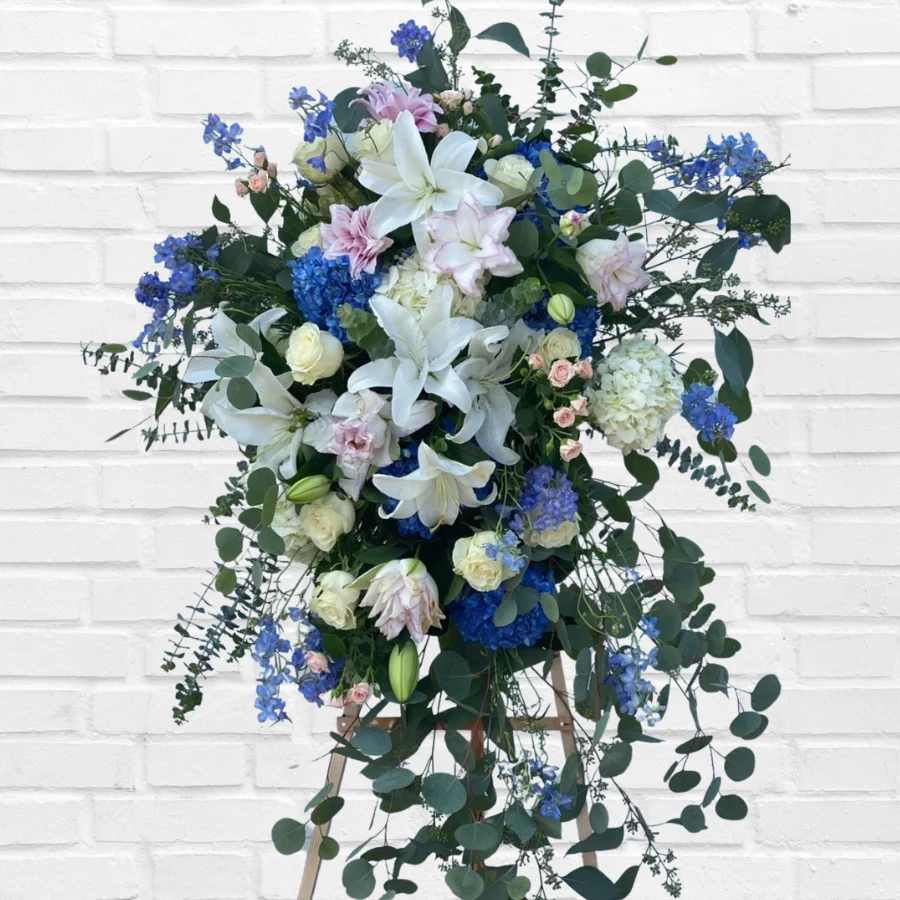 Tall floral spray with white lilies, blue blooms, and trailing greenery on an easel