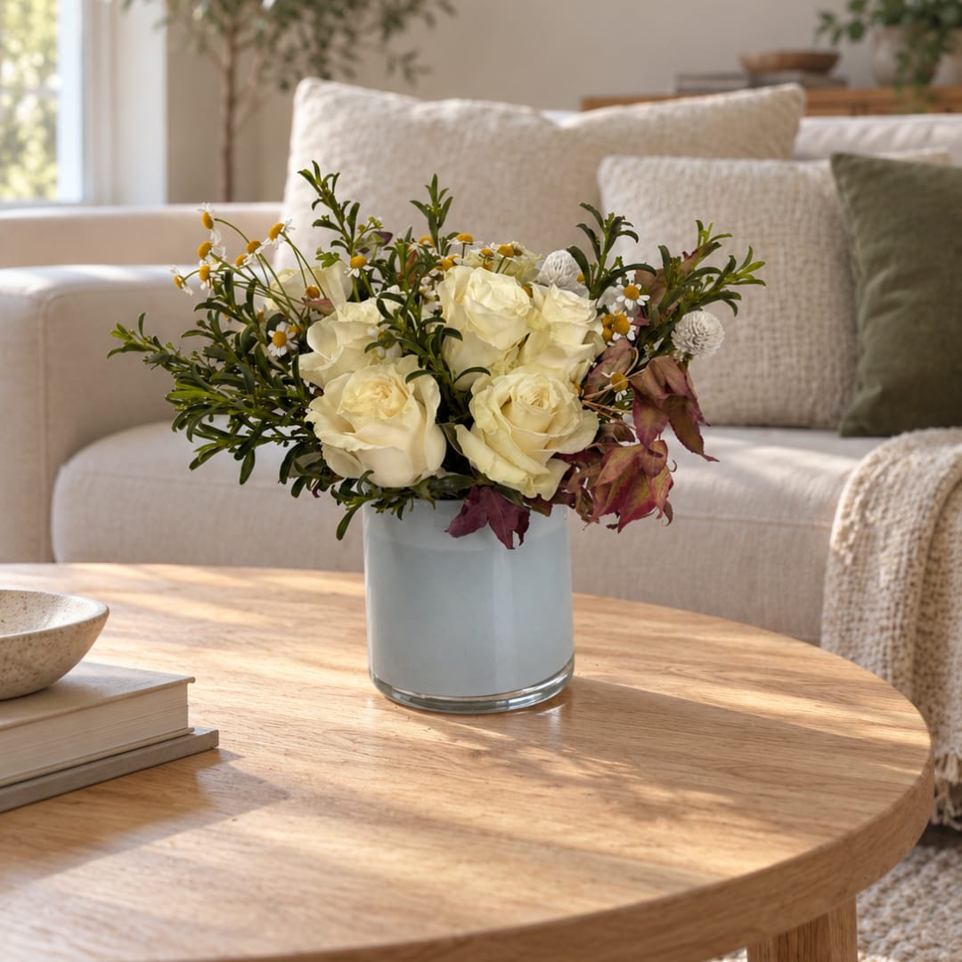 Cream rose bouquet in a light blue glass vase on a coffee table