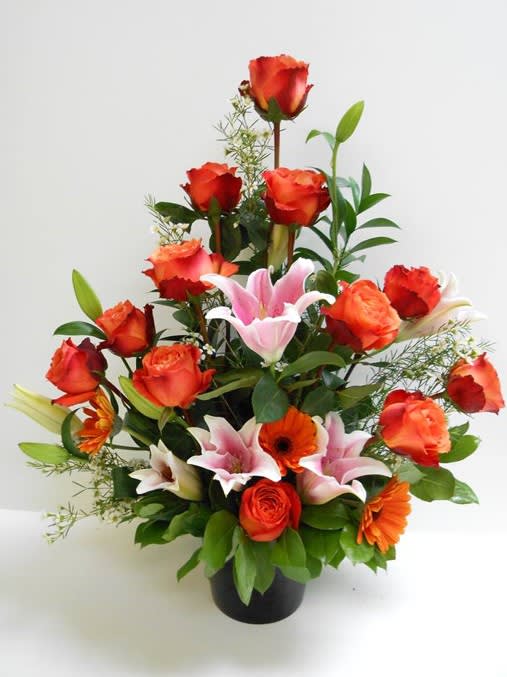 Tall arrangement of orange roses, pink lilies, and orange gerbera daisies in a black vase