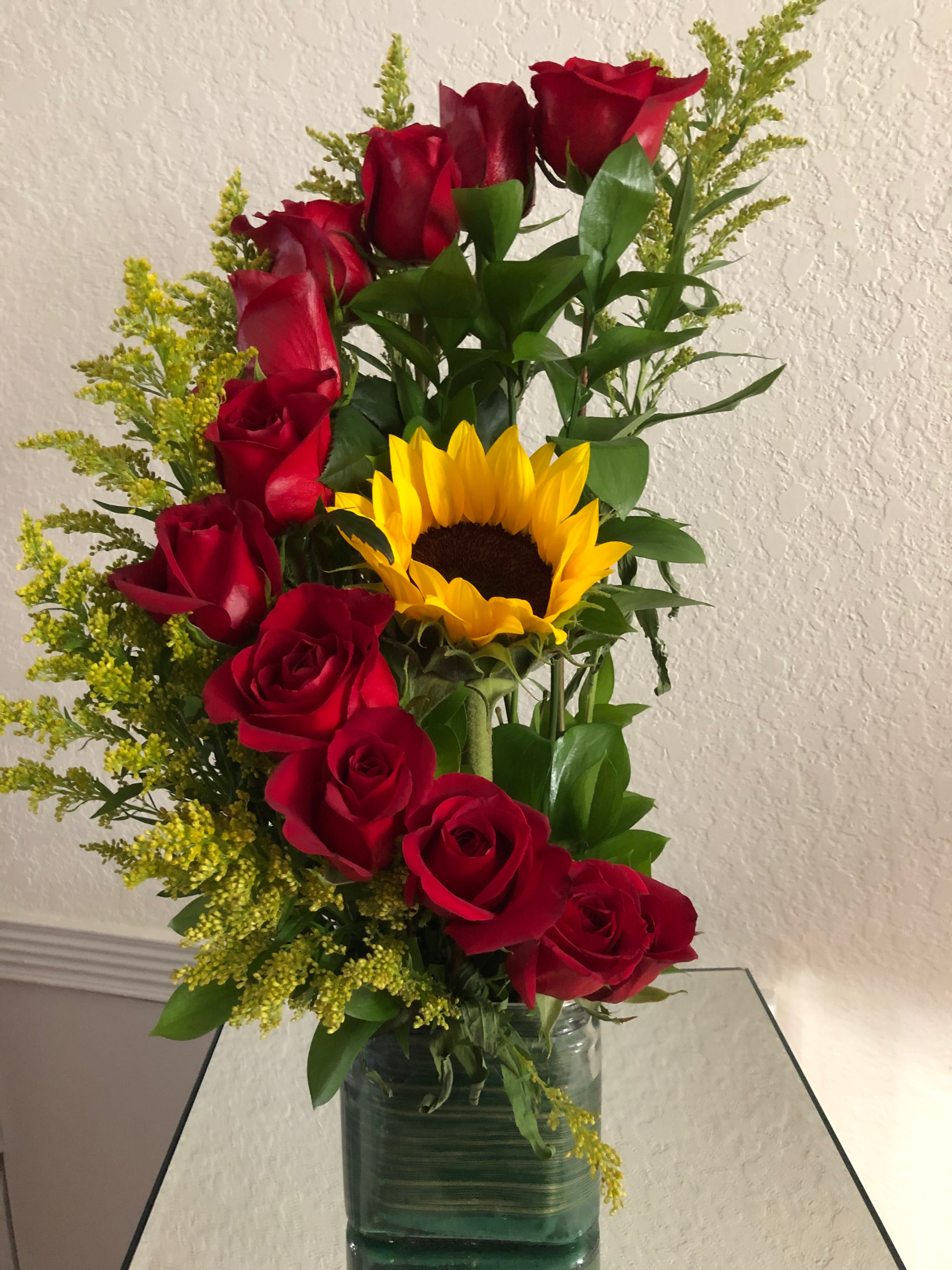 Arrangement of red roses and a yellow sunflower in a green glass vase