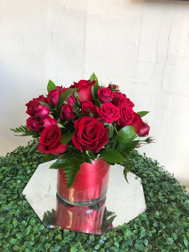 Round arrangement of red roses in a glass cylinder vase on a mirrored base