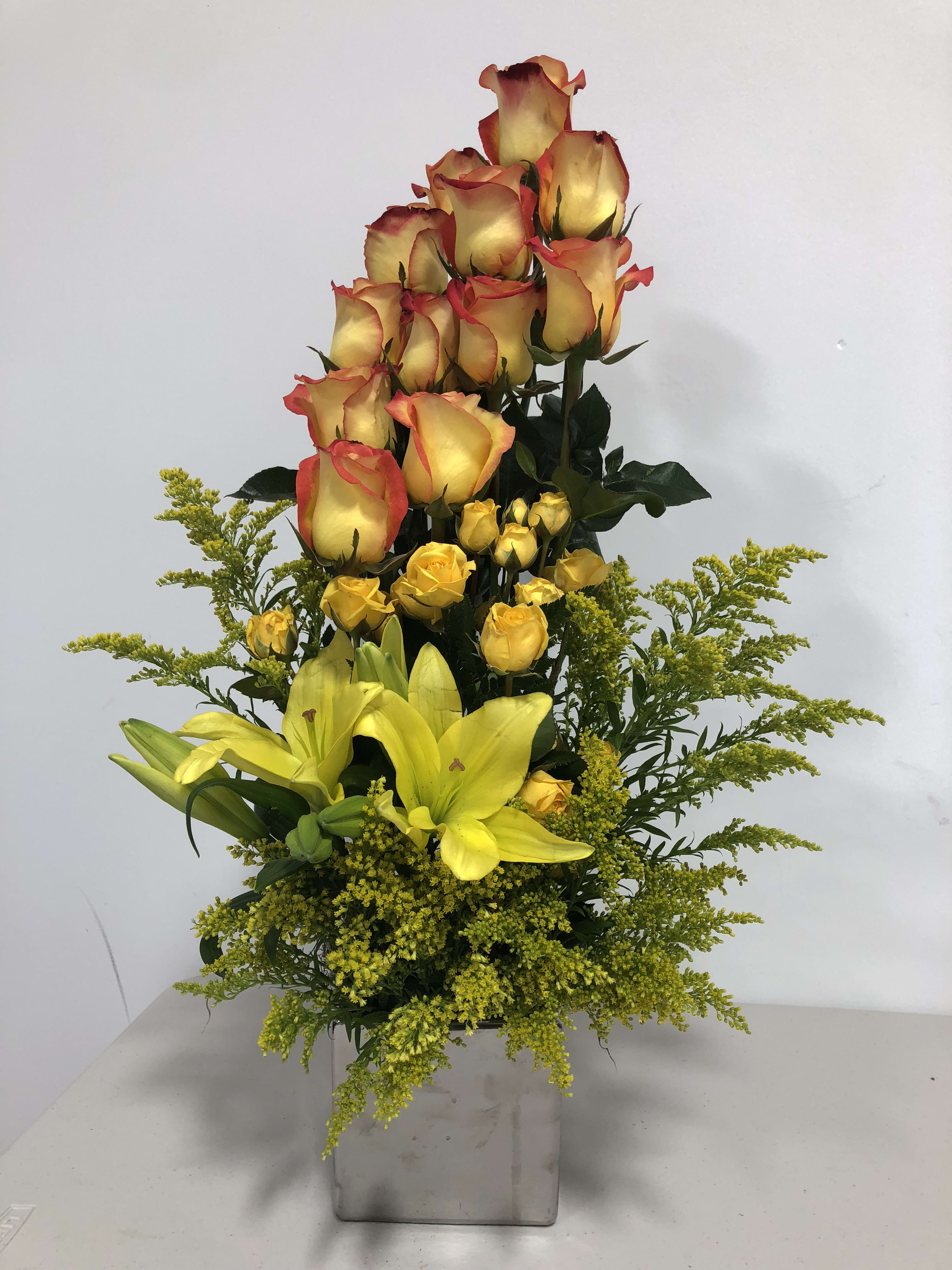 Tall arrangement of yellow lilies and yellow-red roses in a square vase