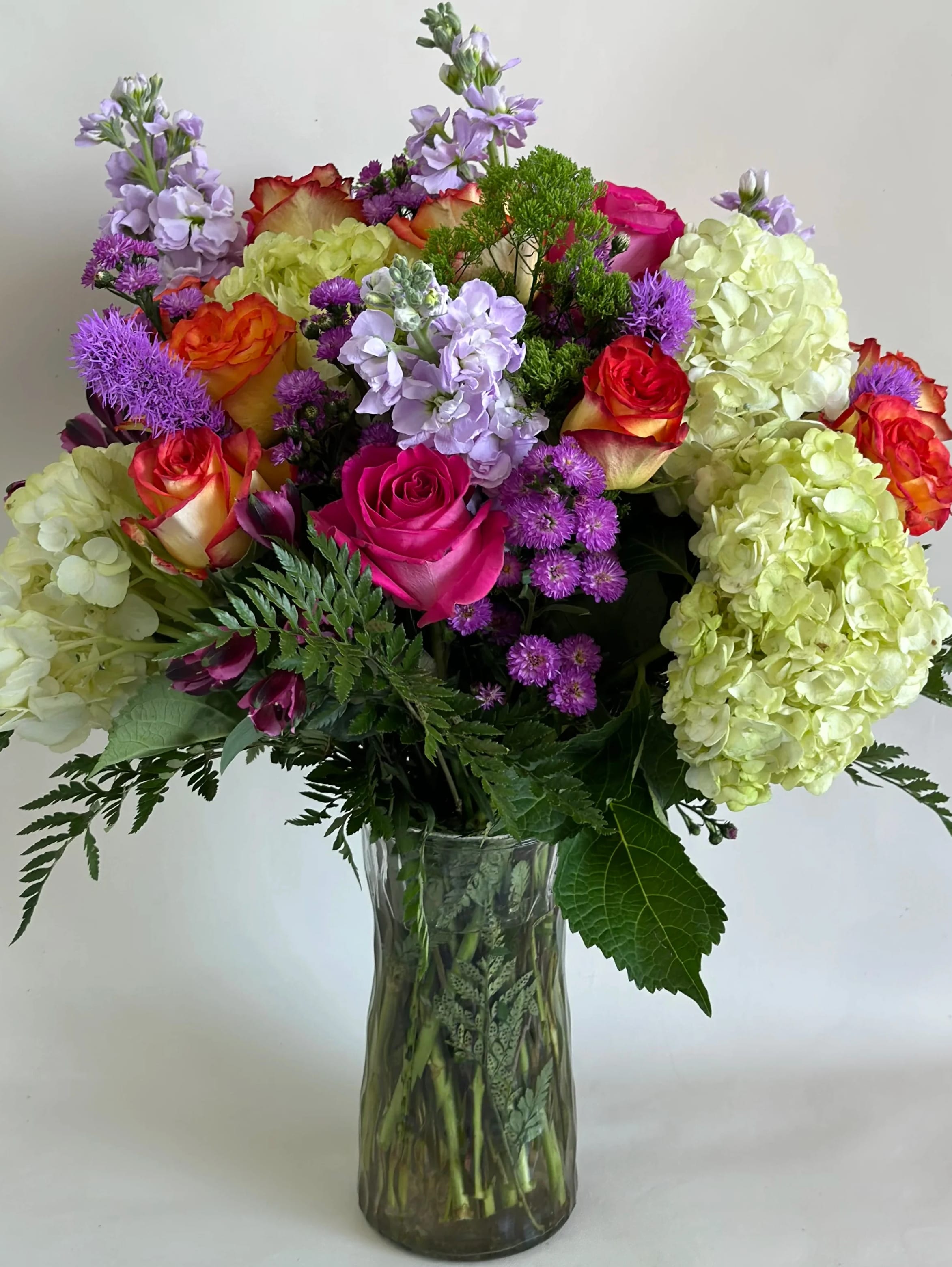 Mixed bouquet of roses, hydrangeas, and purple flowers in a glass vase