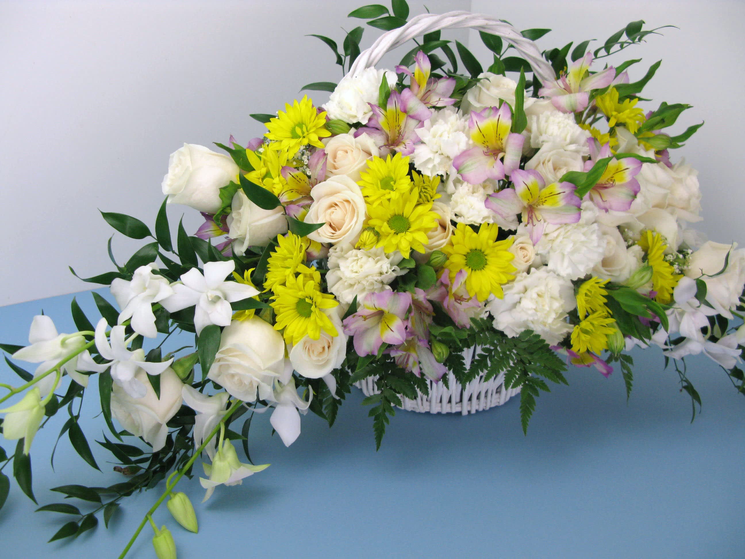 White basket arrangement with white roses, yellow daisies, pink alstroemeria, and orchids