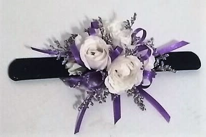 White floral wrist corsage with purple ribbon on a black band