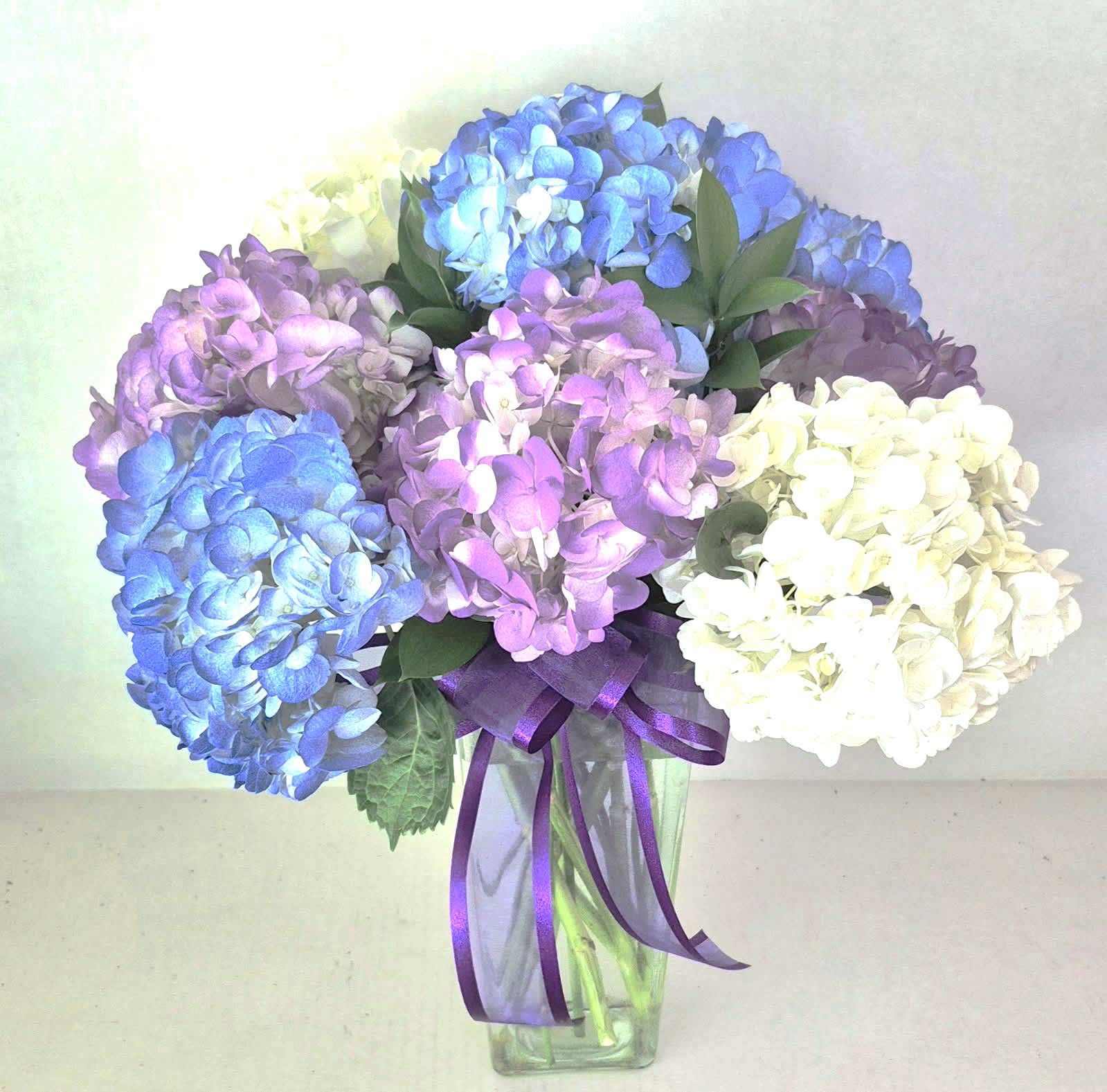 Bouquet of blue, purple, and white hydrangeas in a clear glass vase