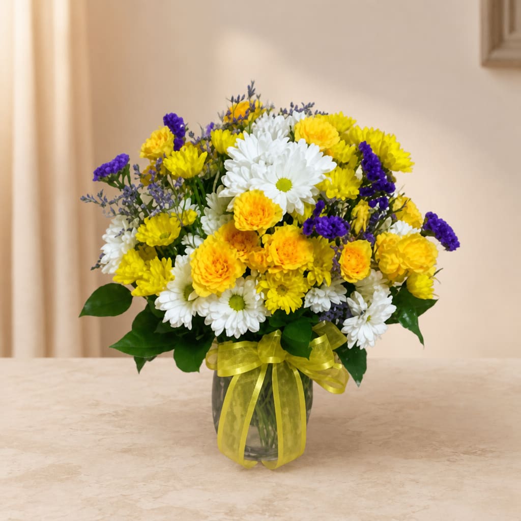 Bouquet of yellow, white, and purple flowers in a glass vase with a yellow ribbon