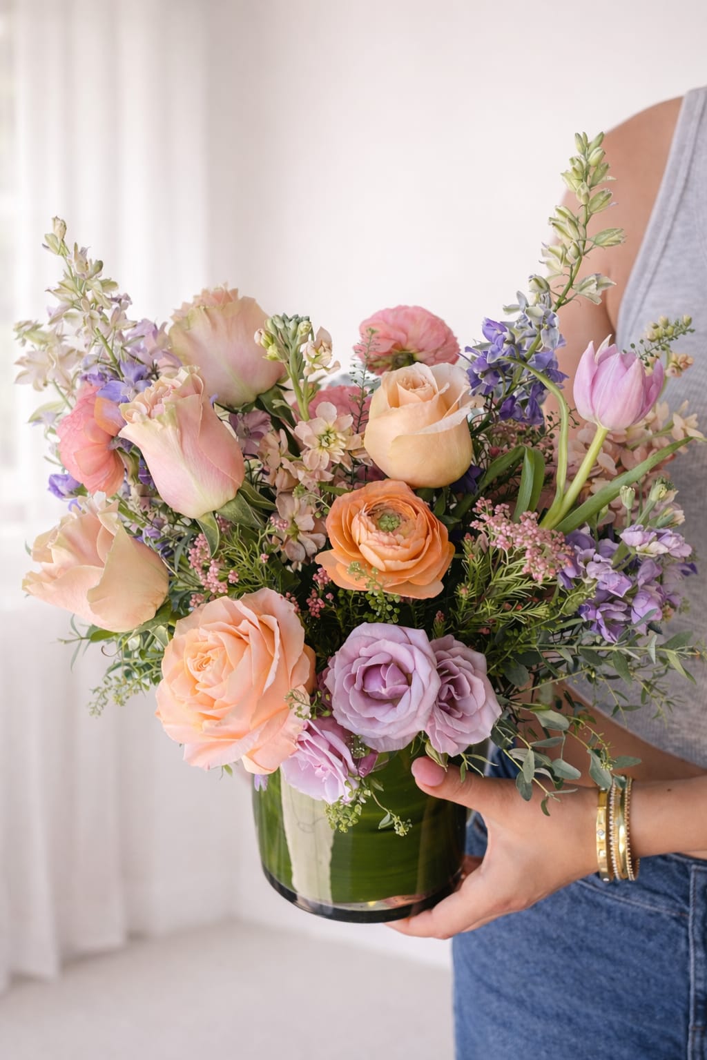 Pastel mixed bouquet of roses, tulips, and purple flowers in a glass vase