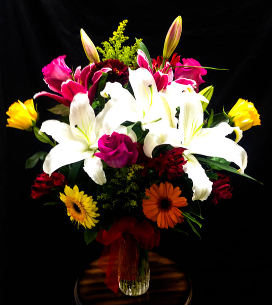 Mixed bouquet with white lilies, pink roses, and gerbera daisies in a glass vase