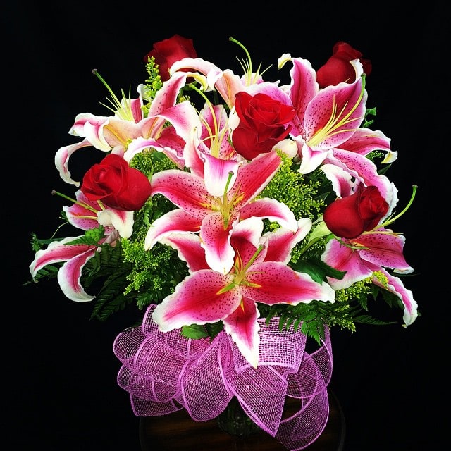 Bouquet of pink lilies and red roses with a purple ribbon wrap