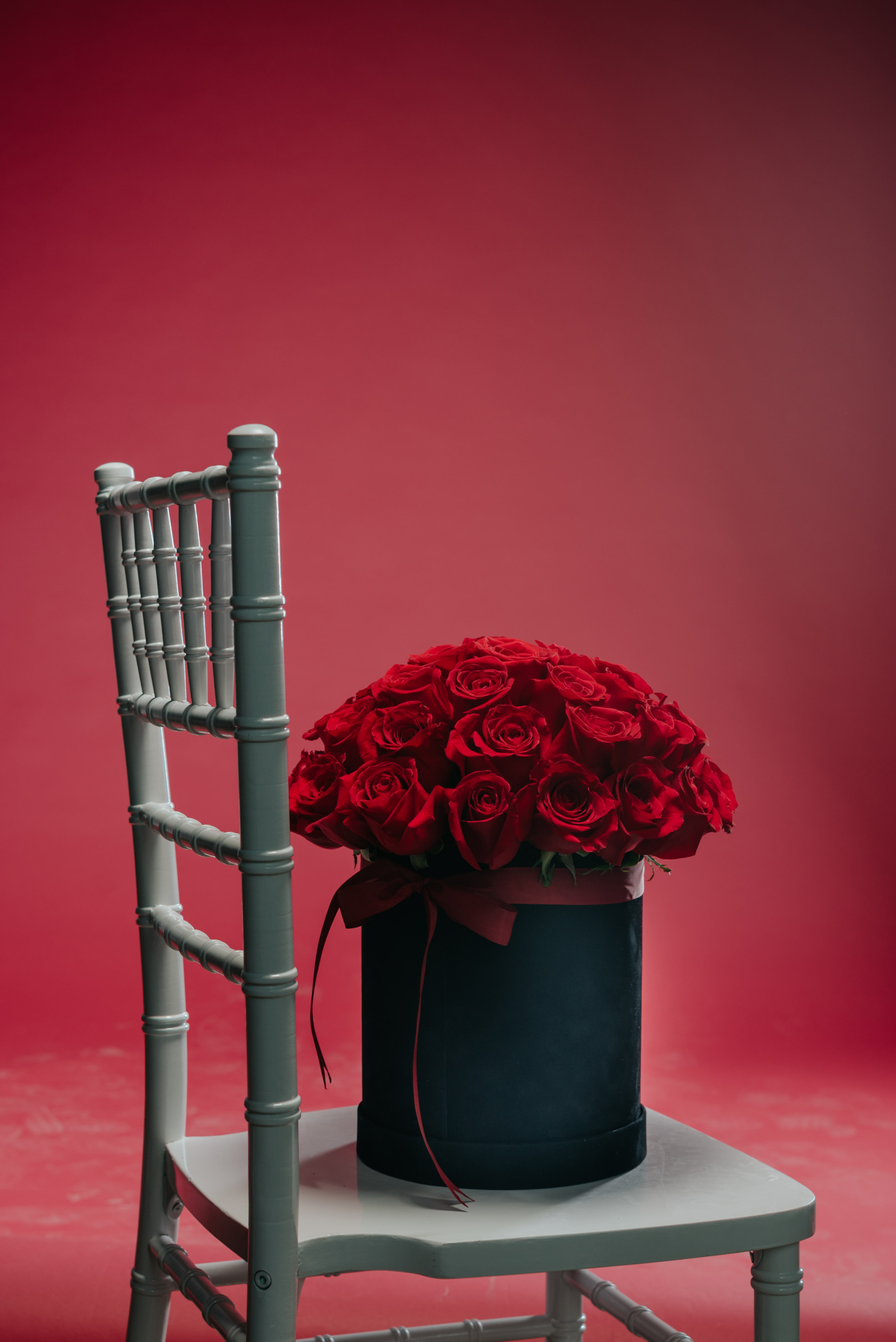 Red rose arrangement in a black hat box on a chair