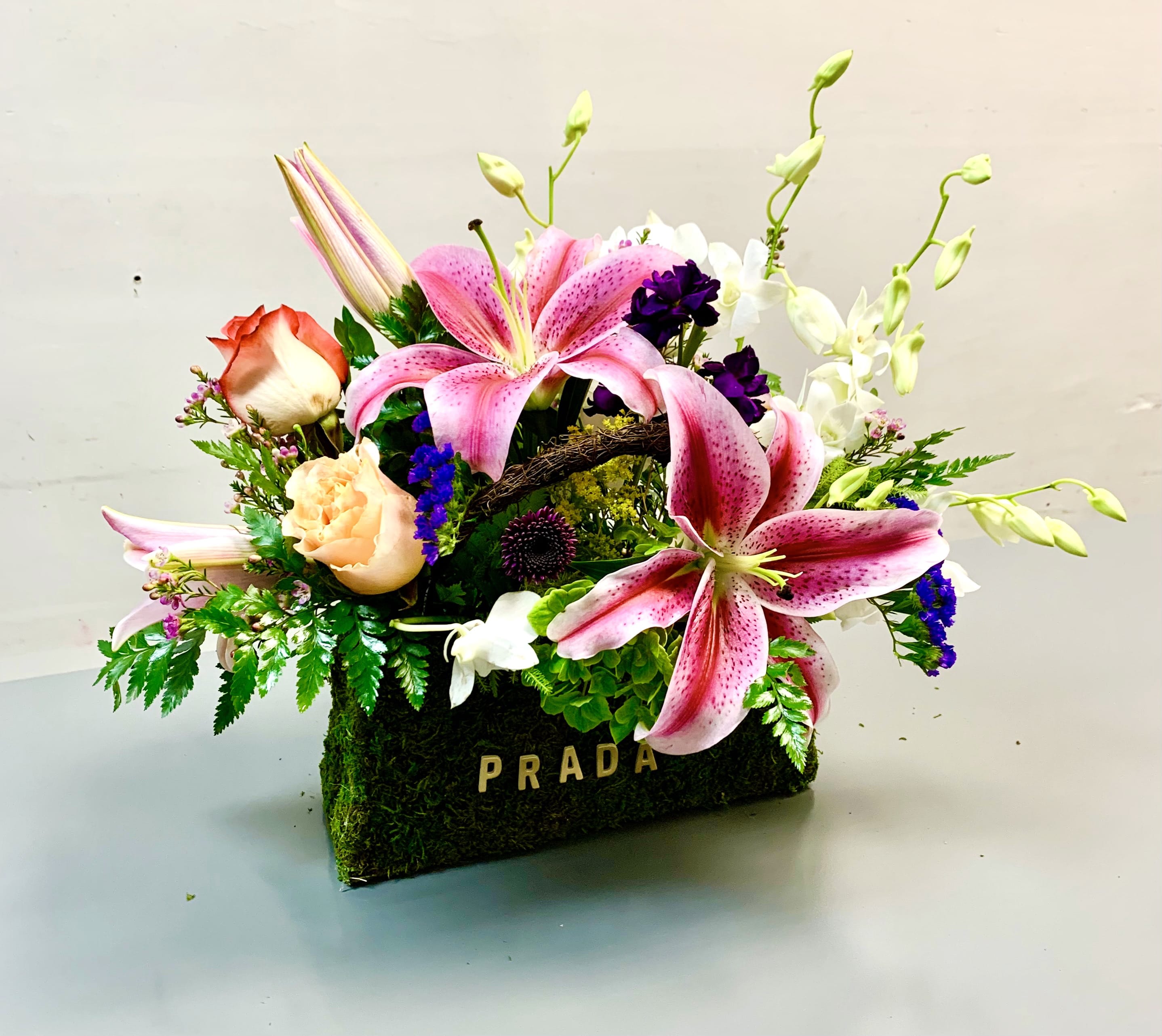 Pink lilies and roses arranged in a moss-covered Prada box