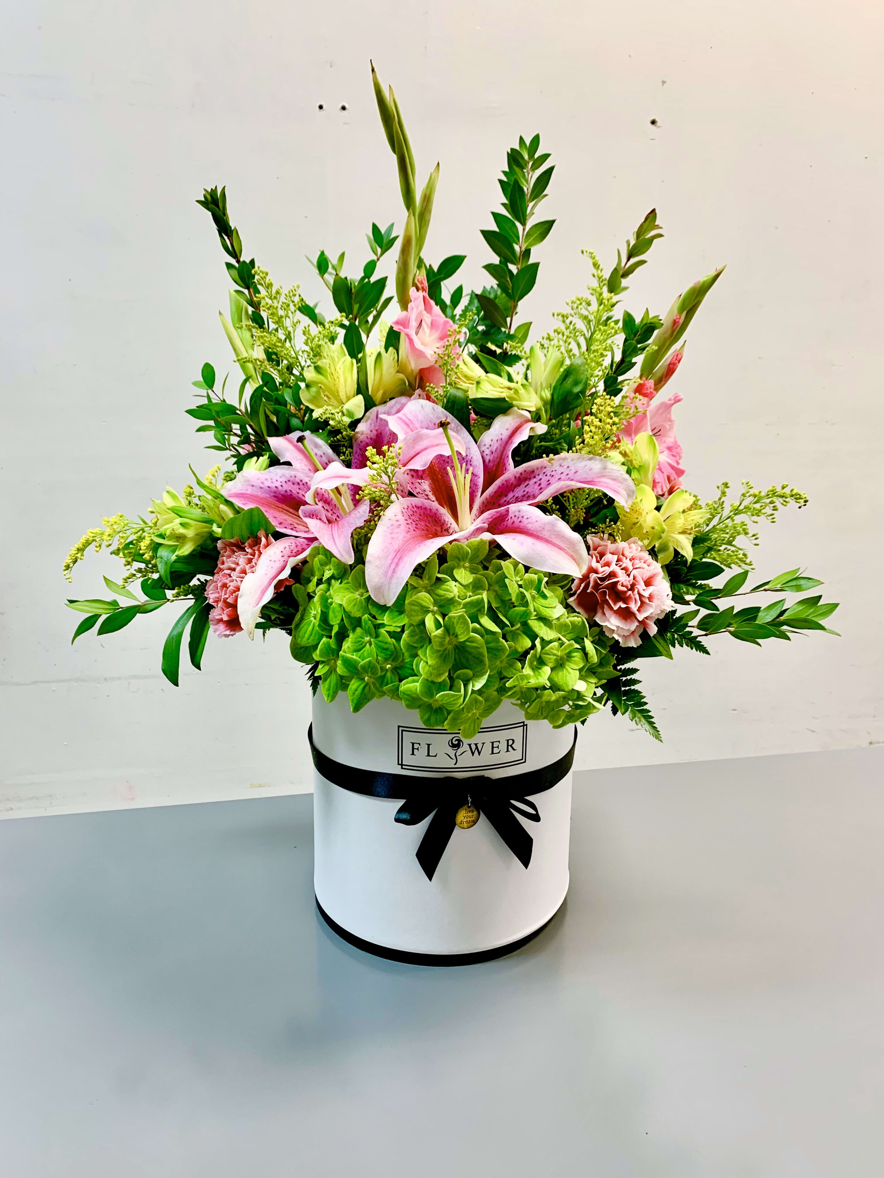 Pink lilies and green hydrangeas in a white hatbox