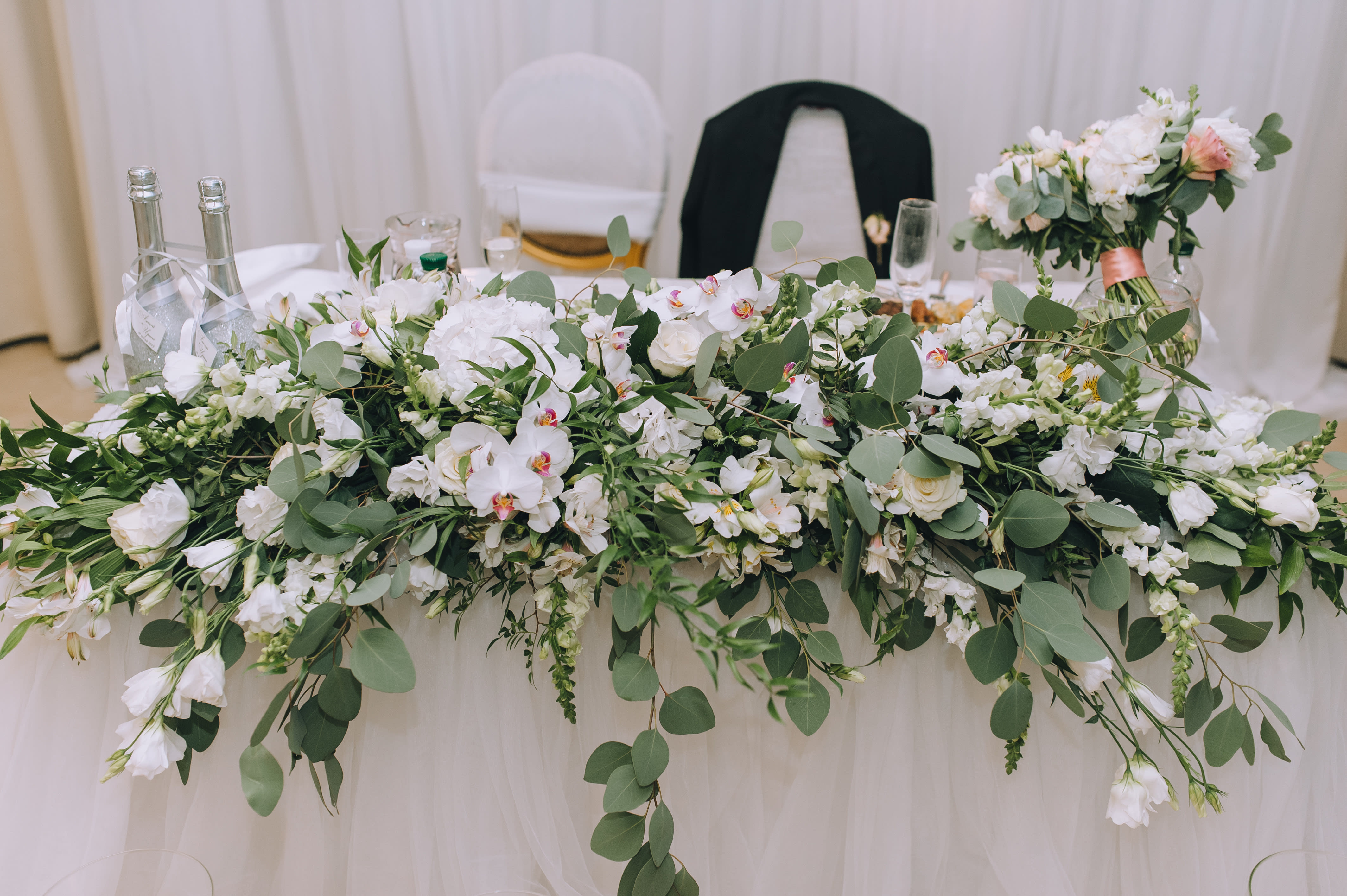 Long white floral centerpiece with greenery on a draped table