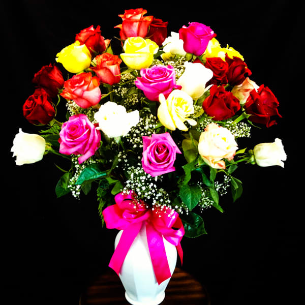 Heart-shaped bouquet of multicolored roses in a white vase with a pink ribbon