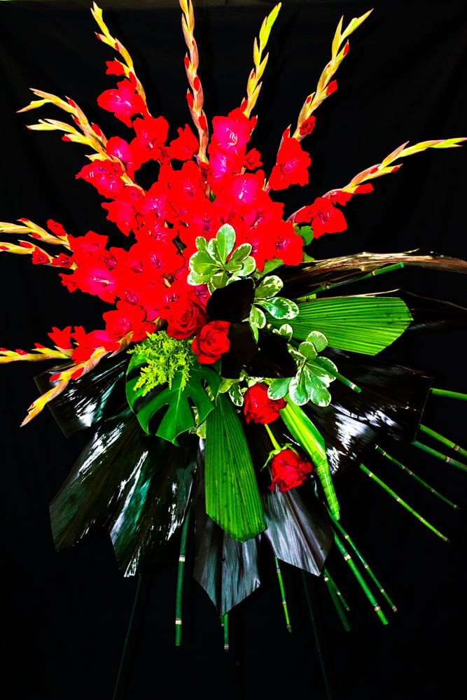Tall red floral arrangement with tropical leaves on a black background