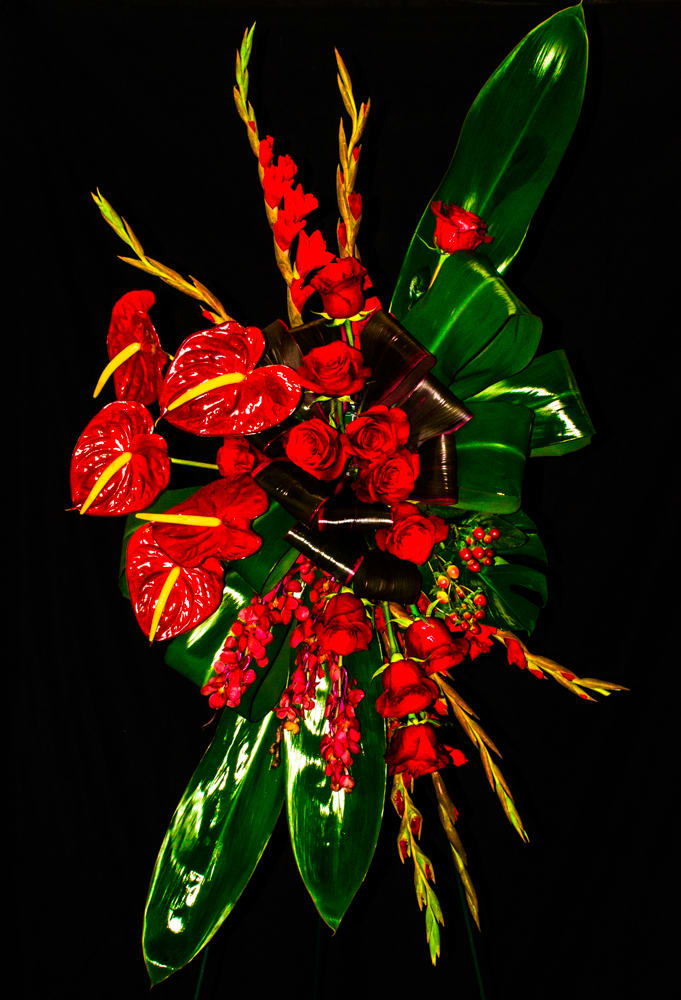 Red roses and tropical flowers with glossy green leaves on a black background