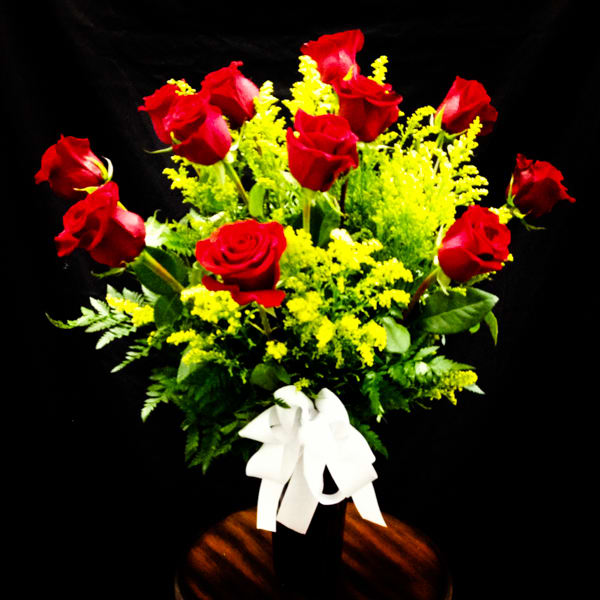 Bouquet of red roses with yellow filler flowers in a vase tied with a white ribbon