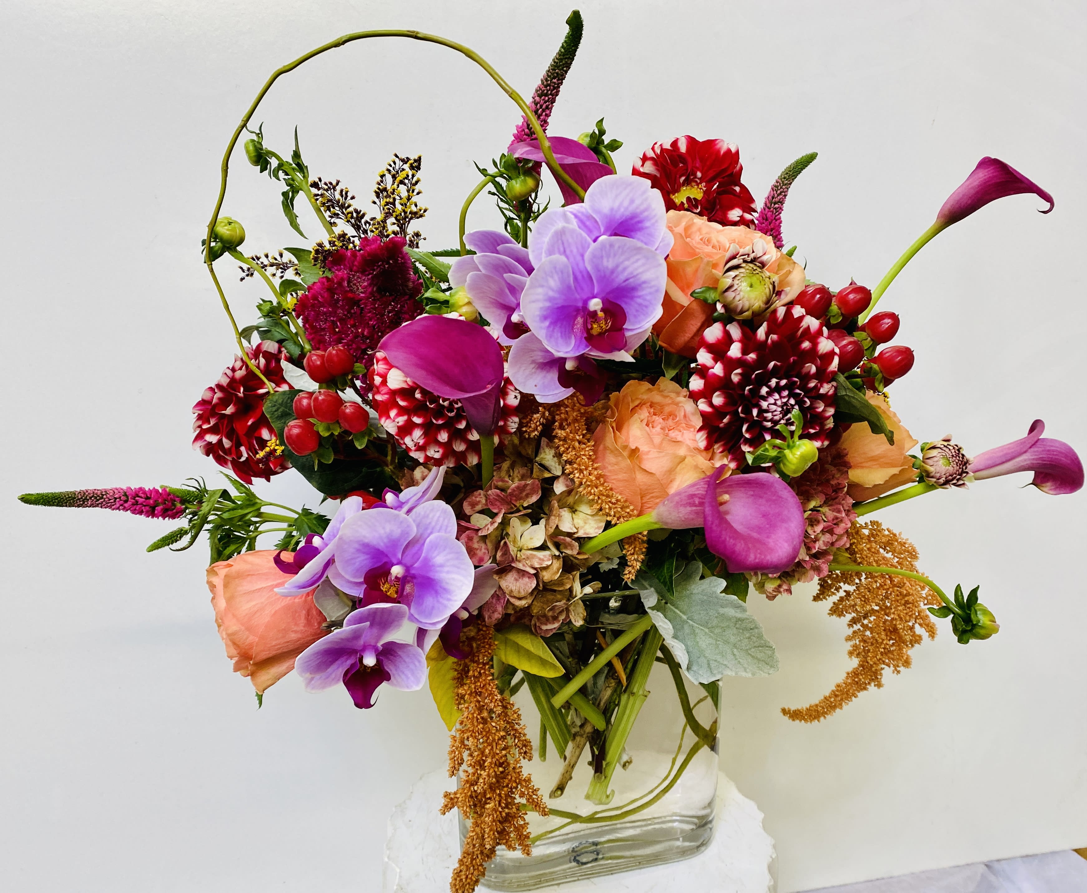 Colorful bouquet with orchids, calla lilies, roses, and dahlias in a glass vase
