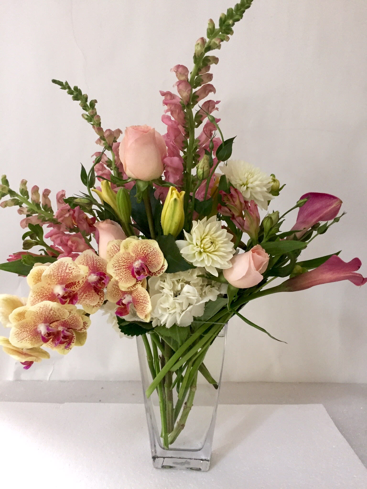 Mixed bouquet in a clear glass vase with pink roses, orchids, and white blooms