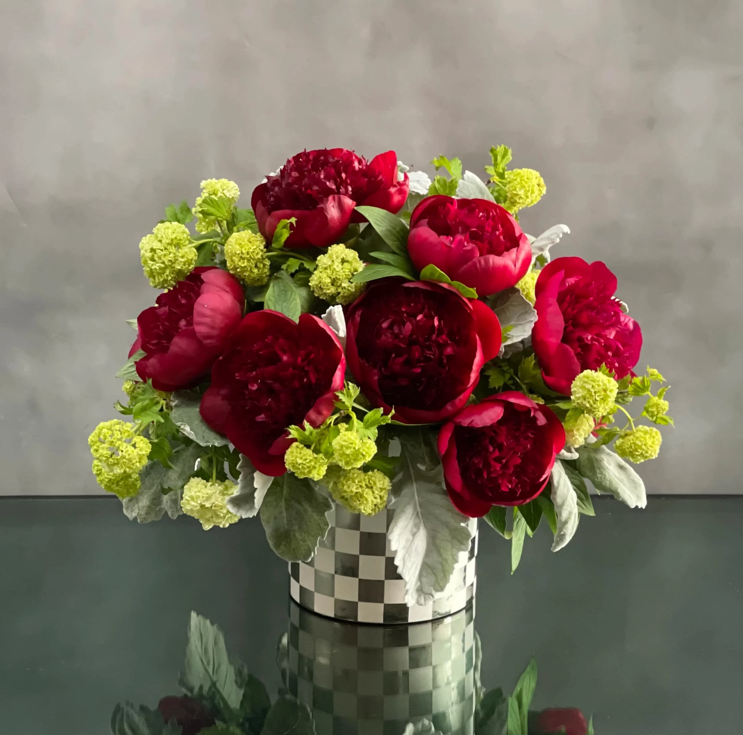 Mackenzie - Motherday Edition  - This arrangement includes rich burgundy peonies with green accents in a shiny checkard vase.