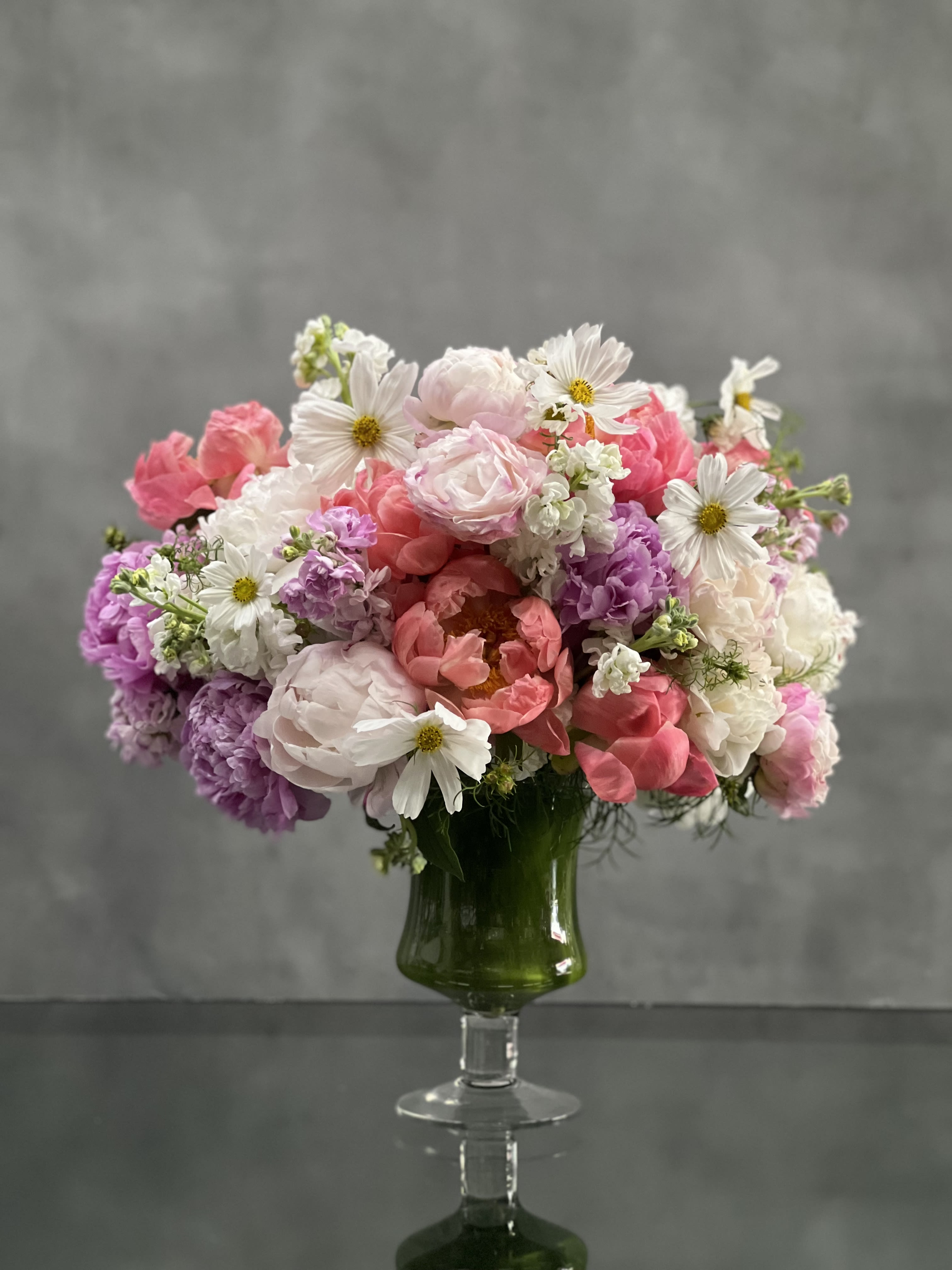 Fanciful Pinks - This pedestal glass vase bursts with bloom upon bloom of gorgeous pinks, and sprinkles of white in a stunning and luscious pastel floral design. This artful and impressive arrangement includes fabulous Peonies, Asters, Stock. A floral gift for any occasion that will surely say, “You’re fabulous!”   