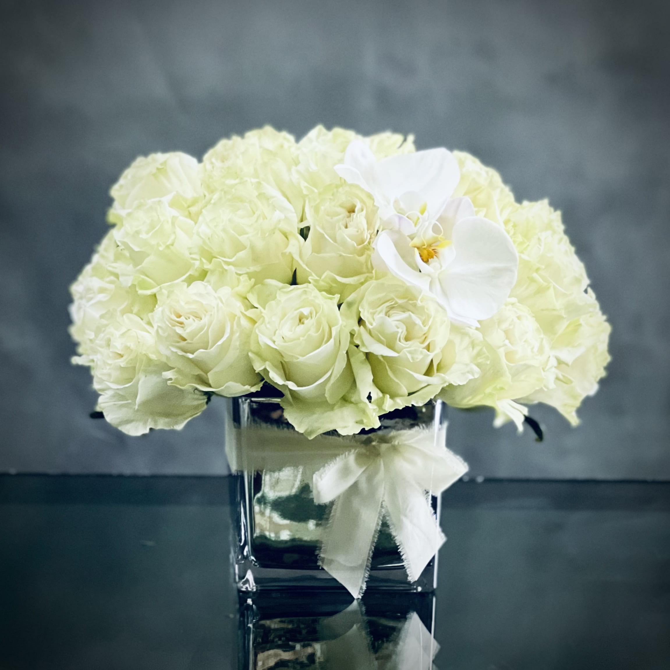 Kissing Butterflies - This arrangement has over 36 Blooms of pale green white Roses accented with kissing White Orchids in a 6 inch Mirrored vase.   approx. 12" Tall and 14" wide 