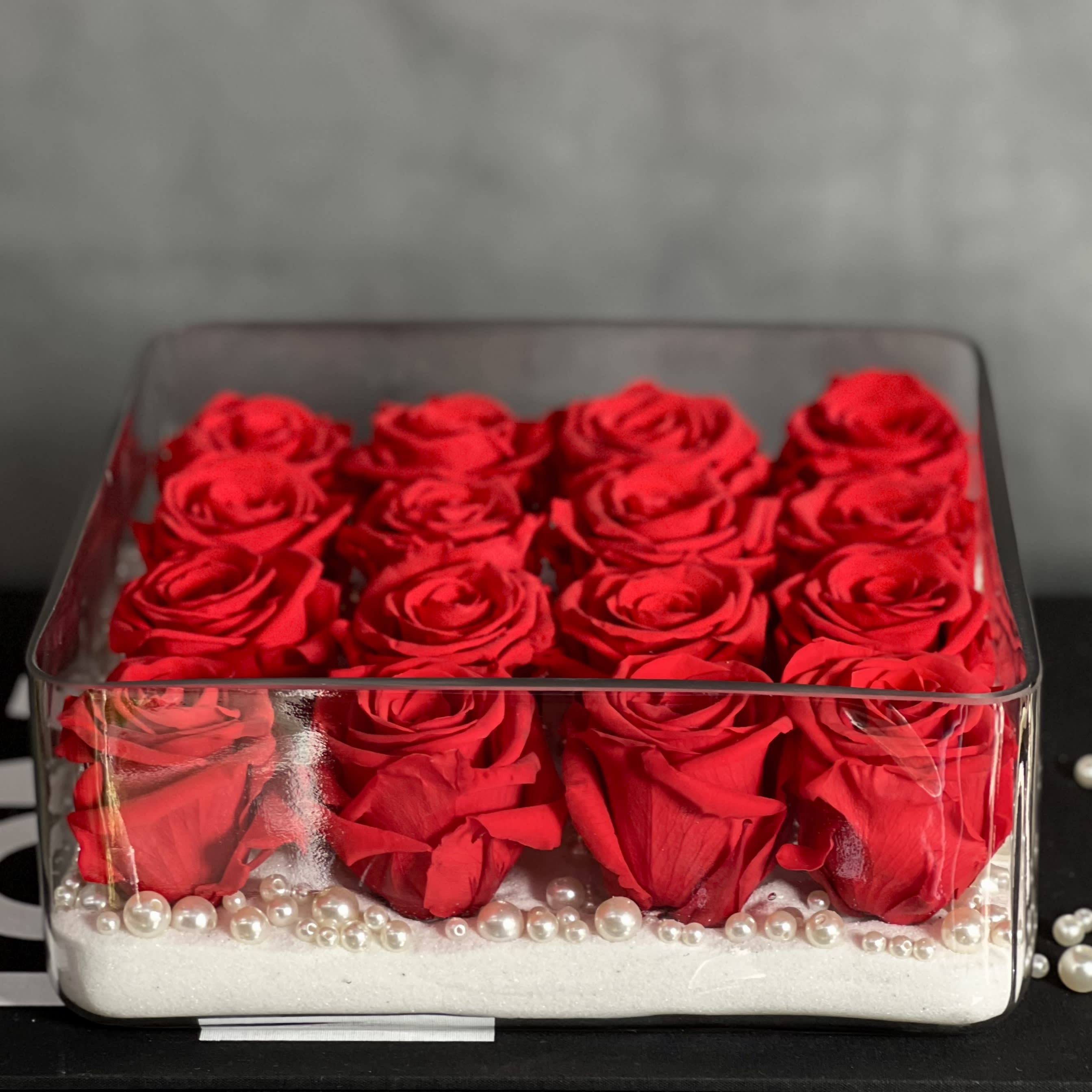 Forever Love's Ashore  - Our "Love's Ashore" is here just in time for Valentine's Day, the perfect way to say I Love You, Just Because or Thinking Of You. In our "Love's Ashore" arrangement is 18 Forever Red Roses placed in a clear glass vase accented with Pearls and white Sand. A simplistic and stunning way to surprise the ones you love.   Measurements:  Arrangement:  10 X 4 