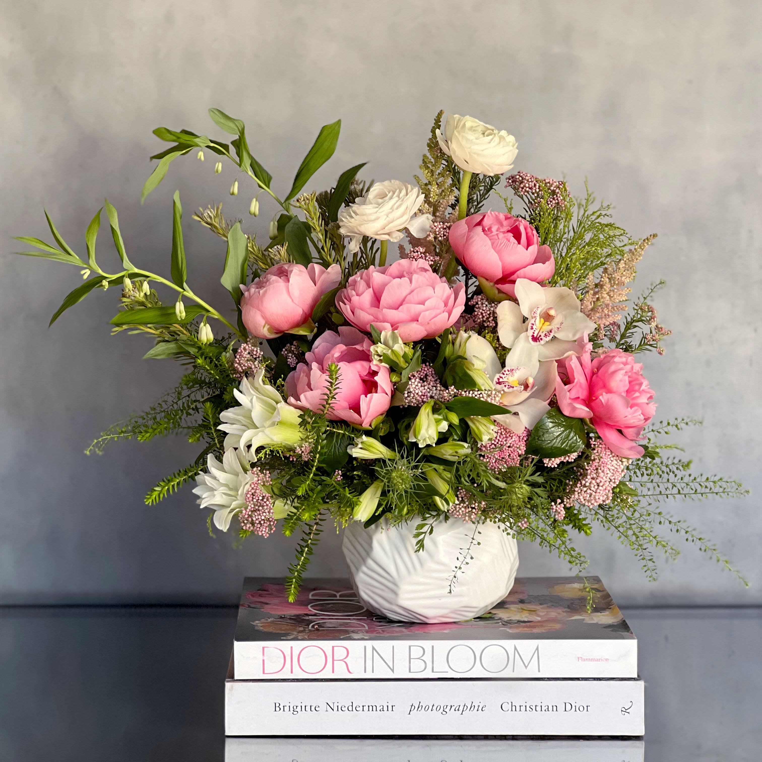 Peony Bunch - Designers Choice -  Experience the pinnacle of luxury with our Blooms and Bliss gift set, now available for same-day delivery in a stunning white ceramic vase, approximately 11 inches tall and 9 inches wide. This exquisite arrangement combines the timeless elegance of peonies with carefully curated elements designed to elevate the senses and create moments of pure indulgence.  At the heart of this opulent ensemble are the breathtaking peonies, meticulously selected for their beauty and freshness. Each bloom exudes a sense of romance and grace, creating a visual masterpiece that captivates the eye and soothes the soul.  Complementing the floral display is a bottle of fine white wine, chosen to enhance moments of relaxation and celebration. Sip and savor the delicate flavors as you immerse yourself in the luxury of the present moment.  But the indulgence doesn't stop there. Our Blooms and Bliss gift set also features rose-infused bath salts, crafted to envelop you in a cloud of soothing fragrance and luxurious hydration. Let the stresses of the day melt away as you indulge in a bath infused with the delicate scent of roses, transporting you to a state of pure tranquility.  To complete this sensory experience, we've included a sumptuous cream, enriched with nourishing ingredients to pamper your skin and leave it feeling soft, supple, and rejuvenated.  With same-day delivery available, you can treat yourself or surprise someone special with this extraordinary gift set, ensuring that the luxury begins without delay. Whether it's a gesture of love, appreciation, or self-care, the Blooms and Bliss gift set promises to deliver moments of pure delight and relaxation that will be cherished long after the flowers have faded. Measurement Approx 14" Tall   