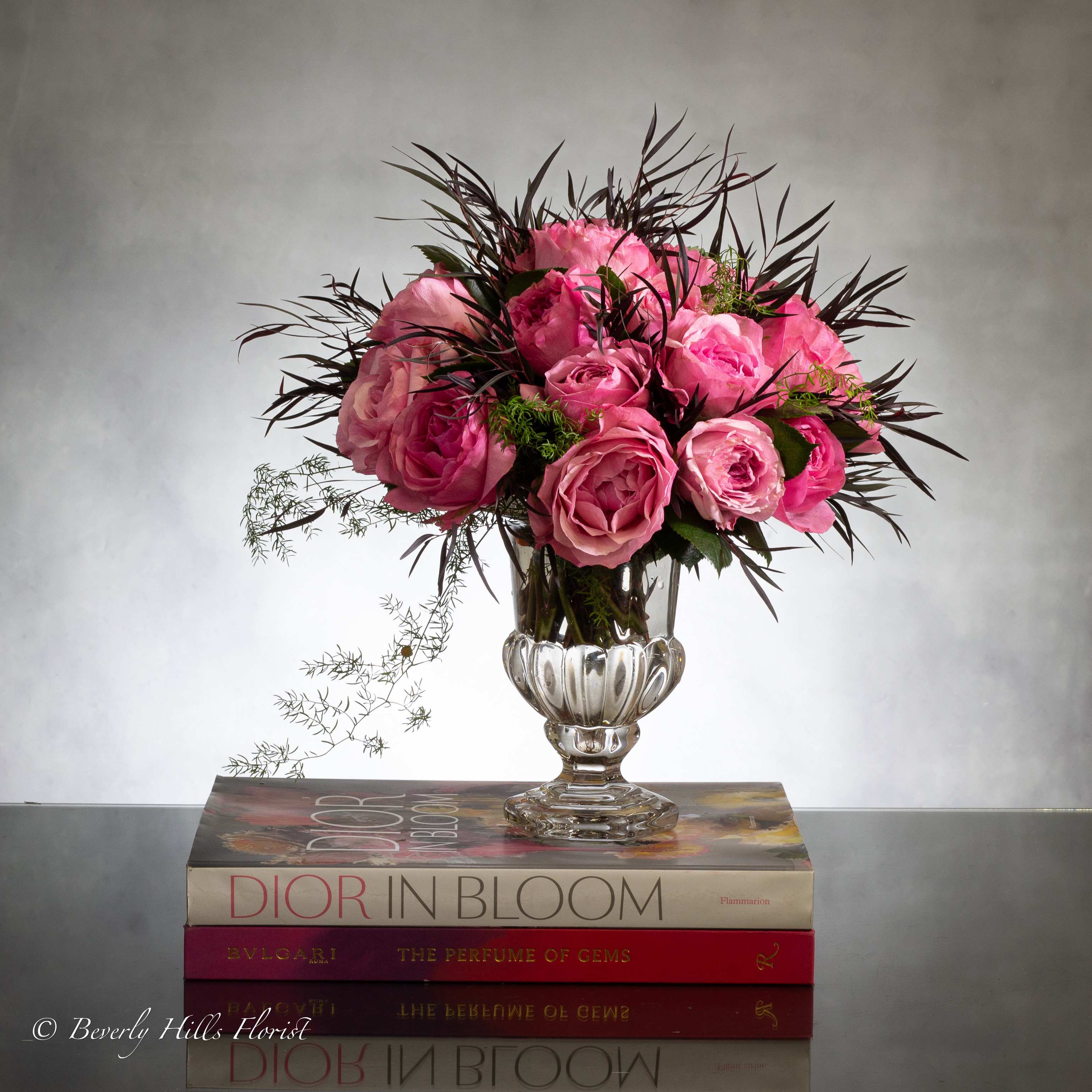 English Garden - Luscious pink roses with seasonal floral and greens in leaf lined footed 7" Footed glass vase. This artistic design is a favorite. This is a grand piece and an amazing gift for any occasion.    MEASUREMENT: 12" TALL   24 Roses As Shown Deluxe