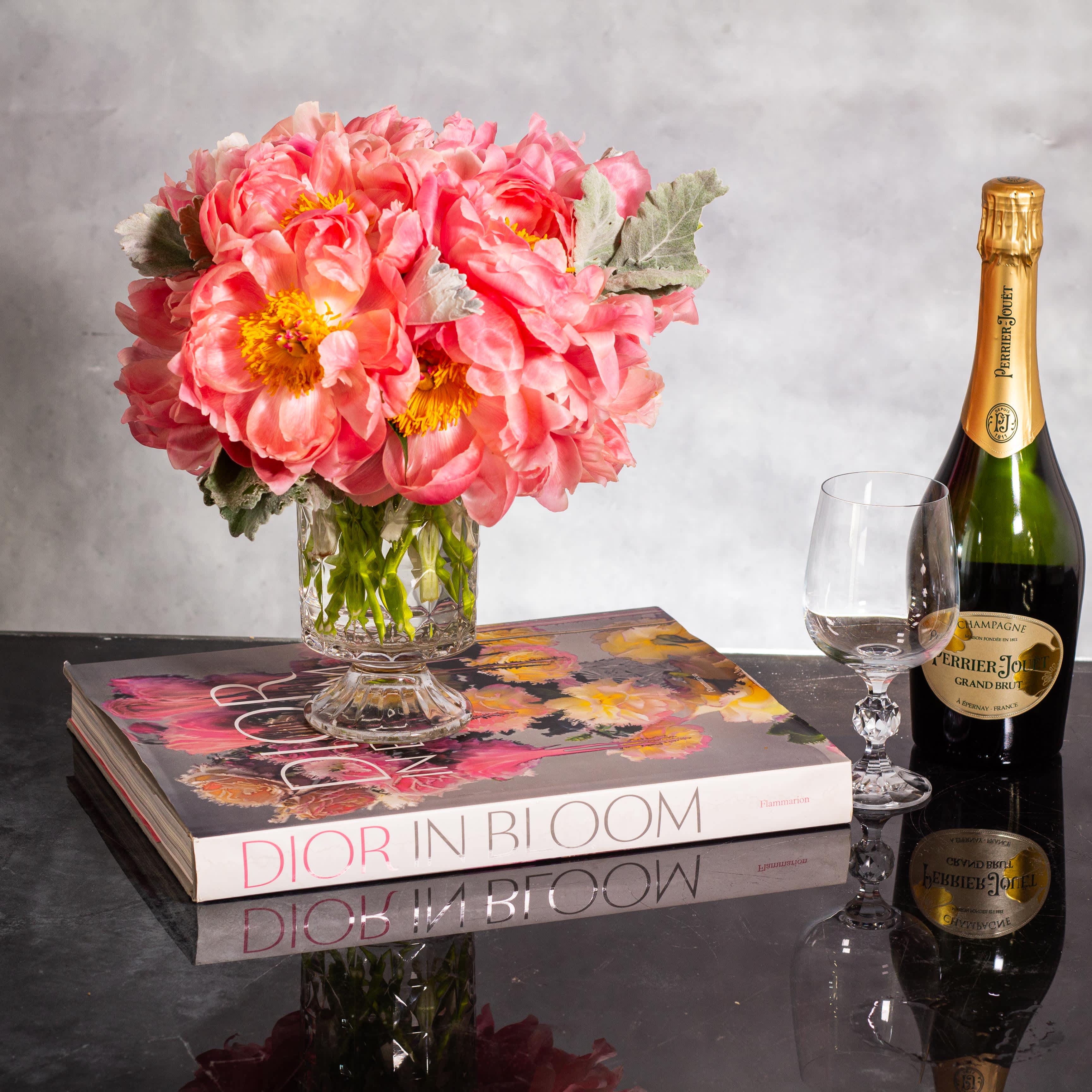 Coral Peony  Embrace - Indulge in the enchanting beauty of our coral color peonies arrangement, delicately nestled in a 7-inch pedestal glass vase. Clusters of vibrant peonies come together to create a stunning display of 18 blooms, celebrating the beauty of nature and the warmth of motherly love. Each peony embodies a message of grace and admiration, making this creation a special gift to honor and cherish our mothers.