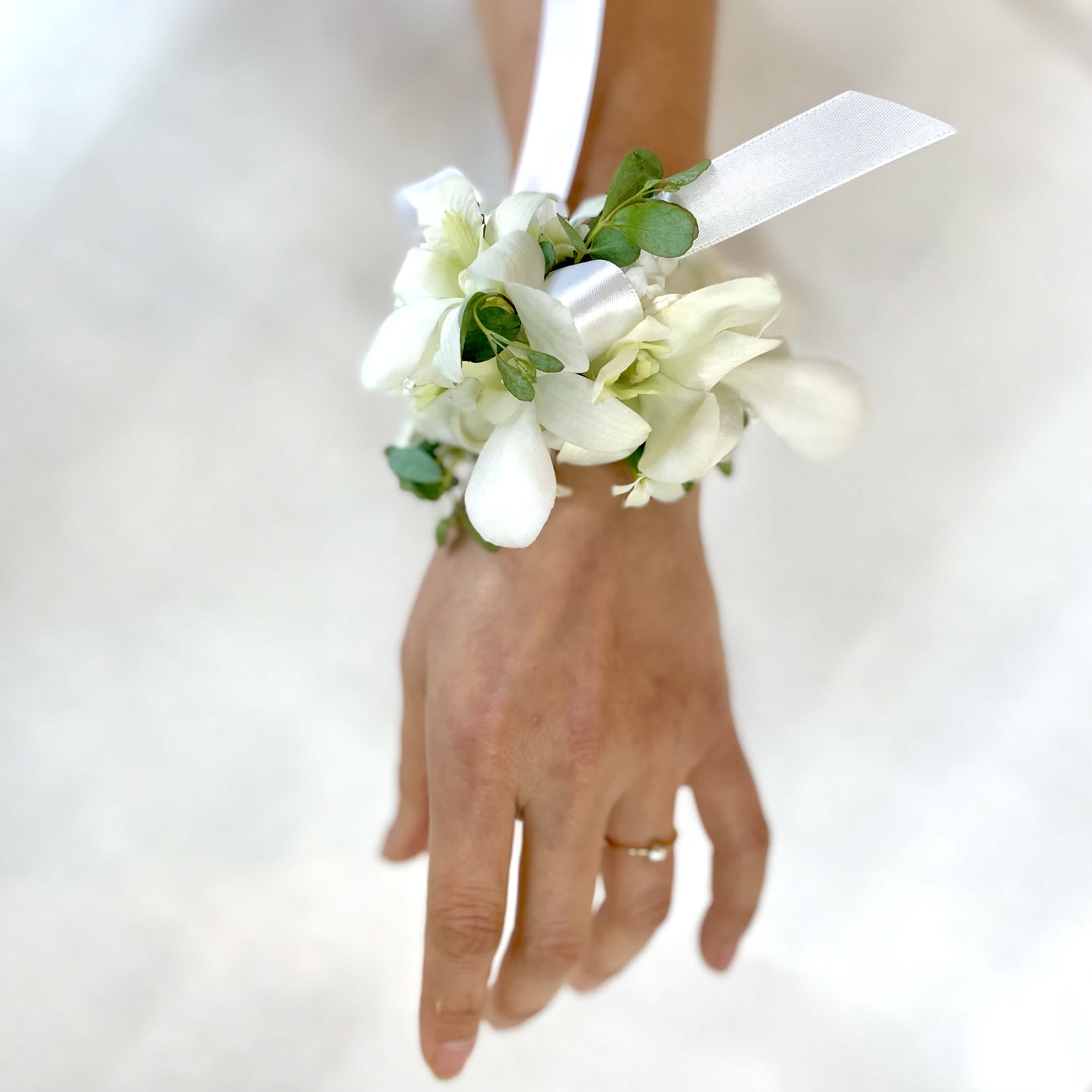 White orchid wrist corsage with ribbon on a person’s hand