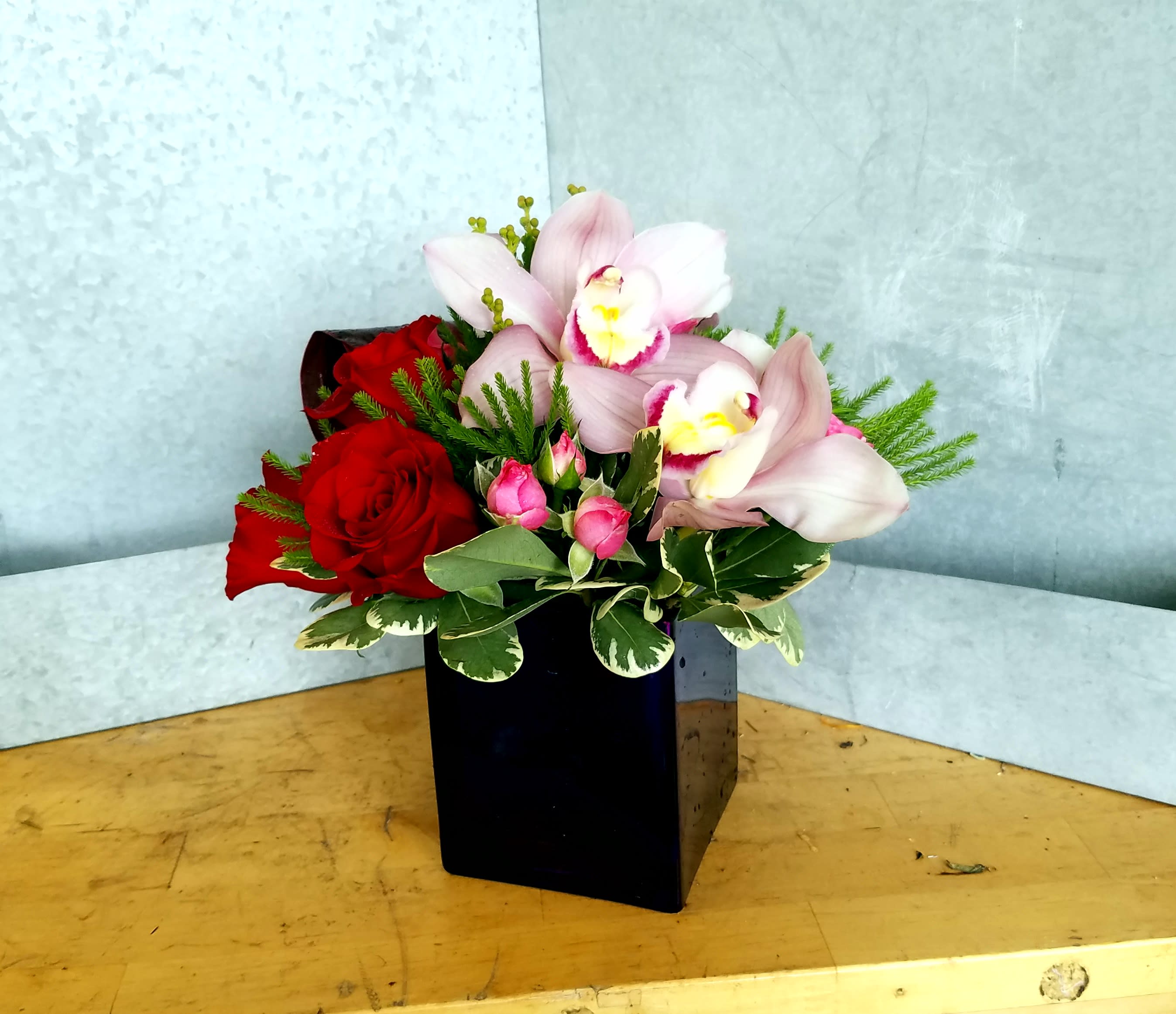 Red roses and pale pink orchids in a black square vase