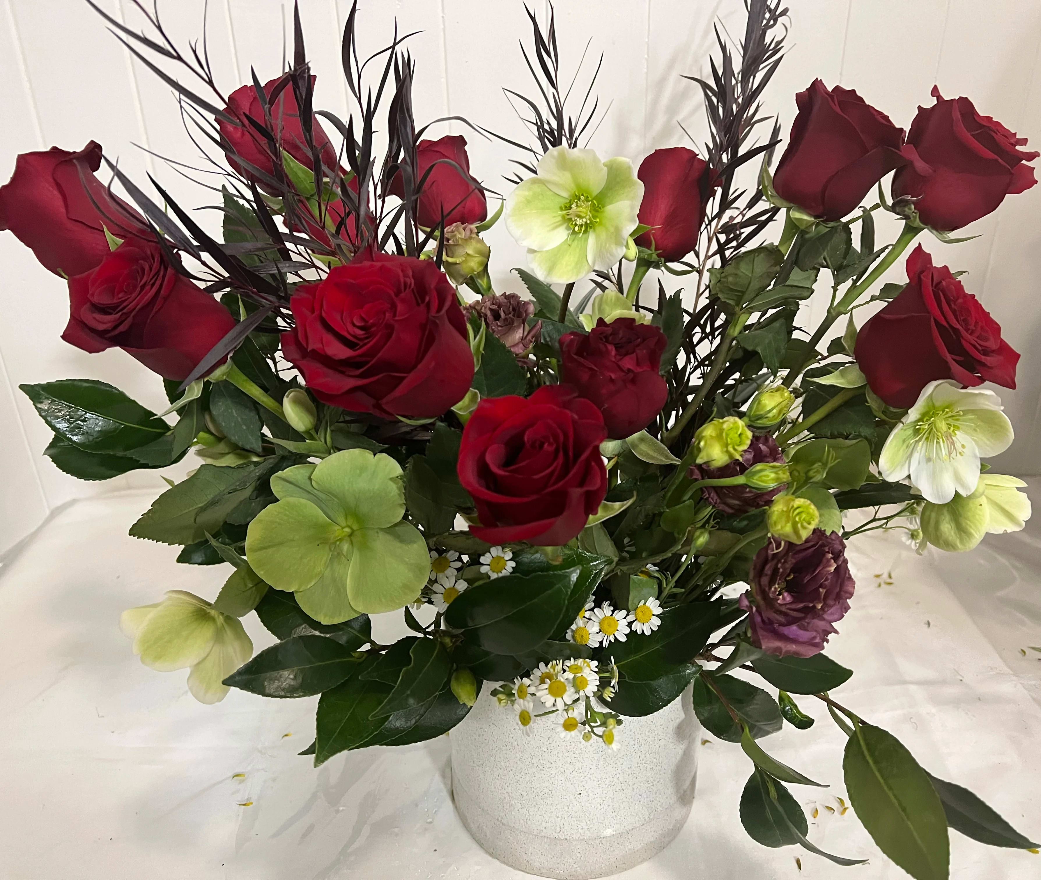Red roses and pale green flowers arranged in a white vase