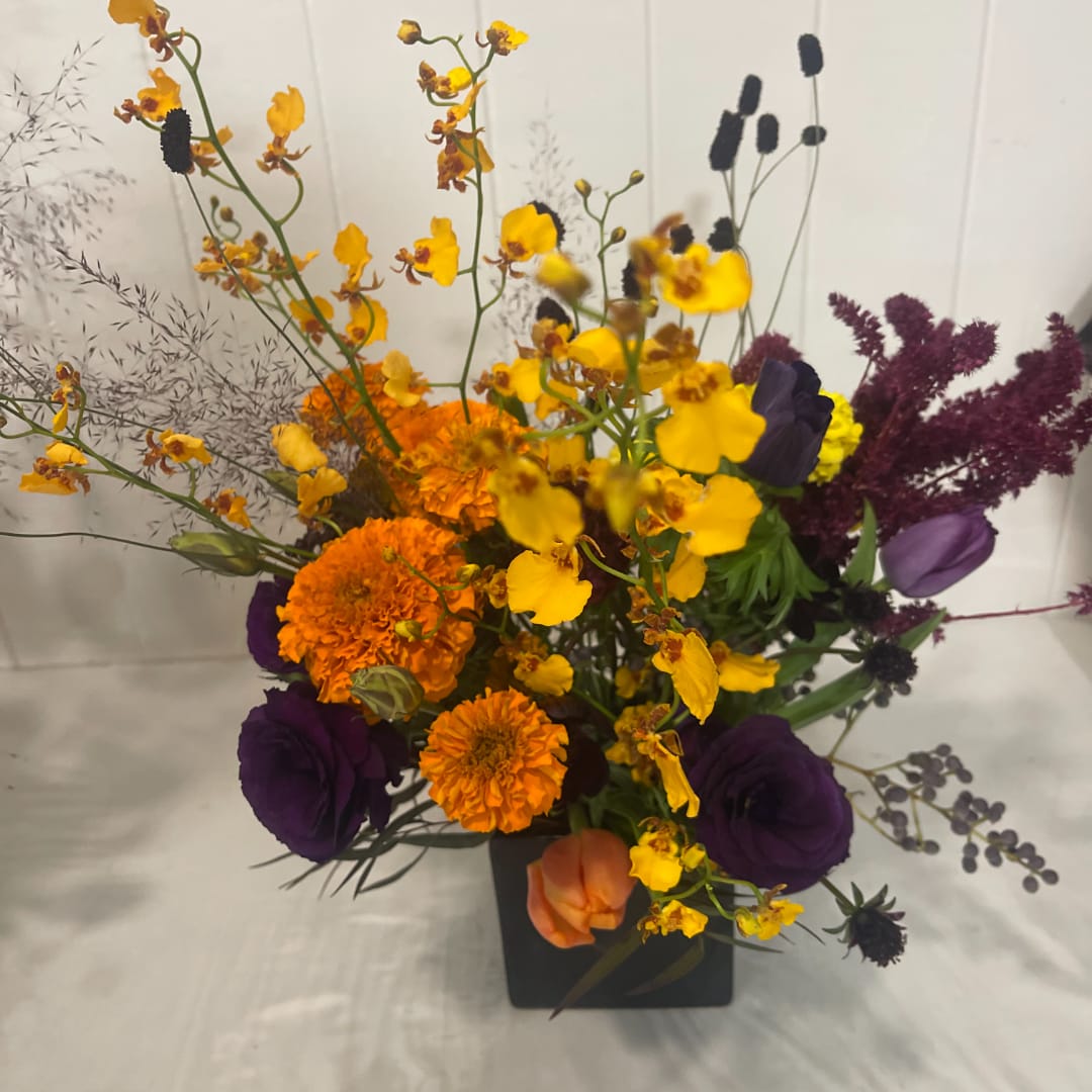 Colorful bouquet with orange, yellow, and purple flowers in a black vase