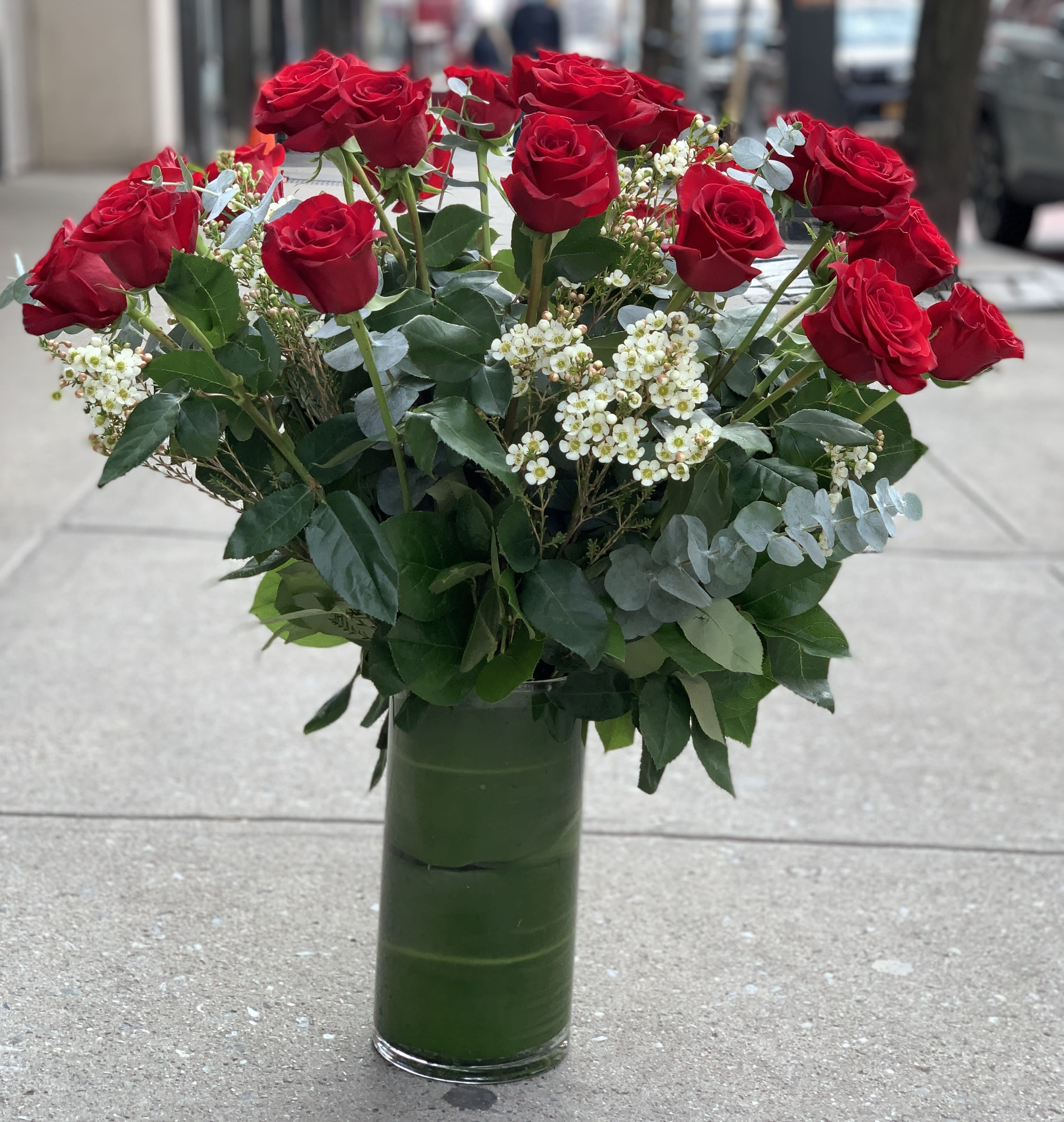Red roses arranged in a tall glass vase with white filler flowers
