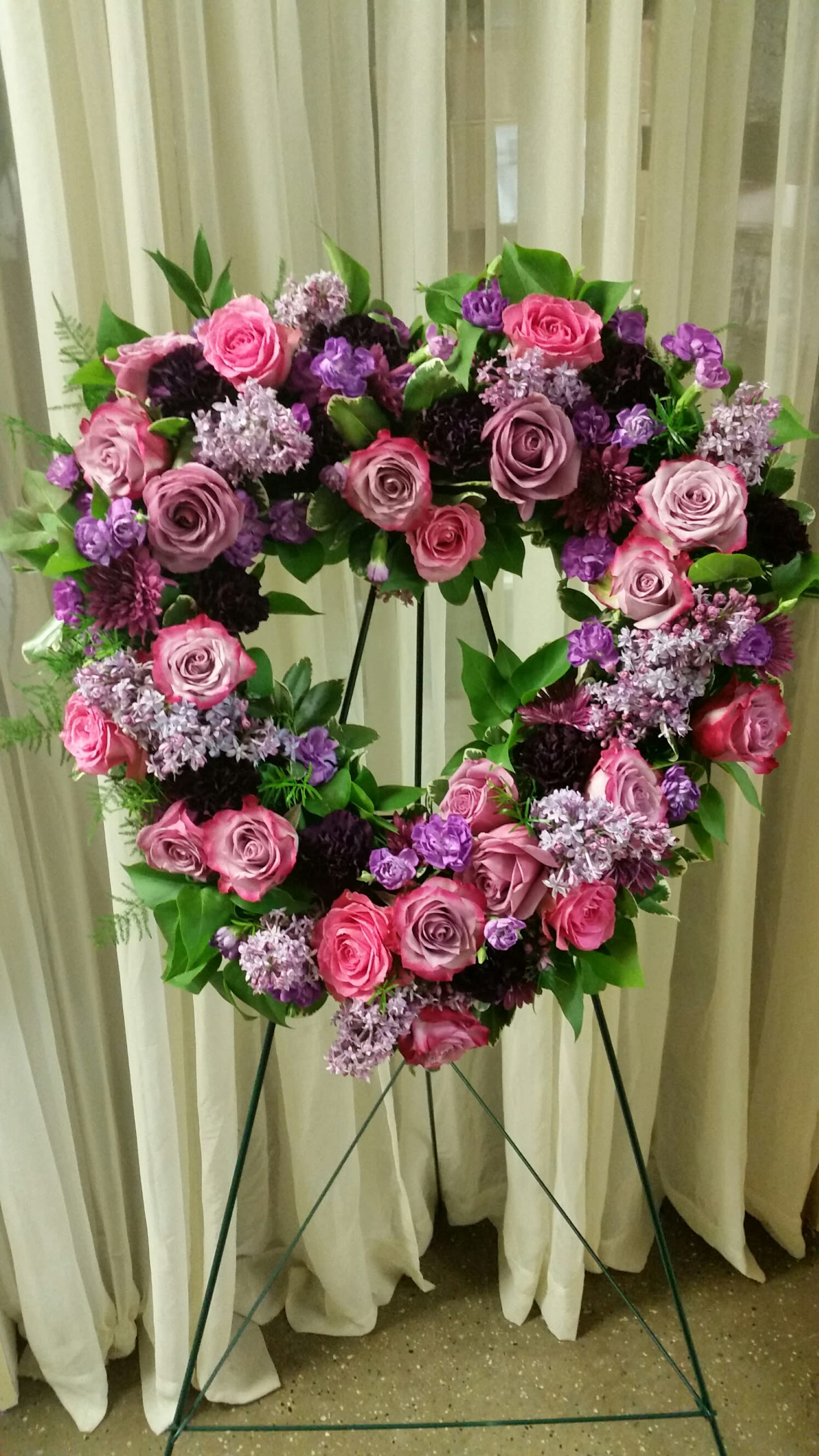 Heart-shaped floral wreath of pink and purple roses on a stand