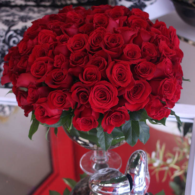 Large dome of red roses arranged in a clear pedestal glass vase