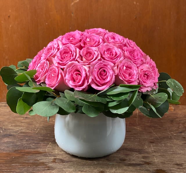 Low dome of bright pink roses with a ring of greenery in a white ceramic vase