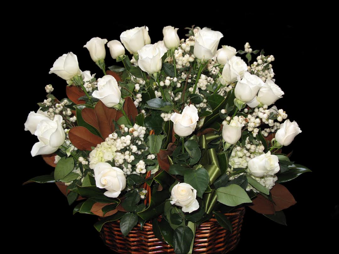 Basket arrangement of white roses and white berries in a brown basket against a black background