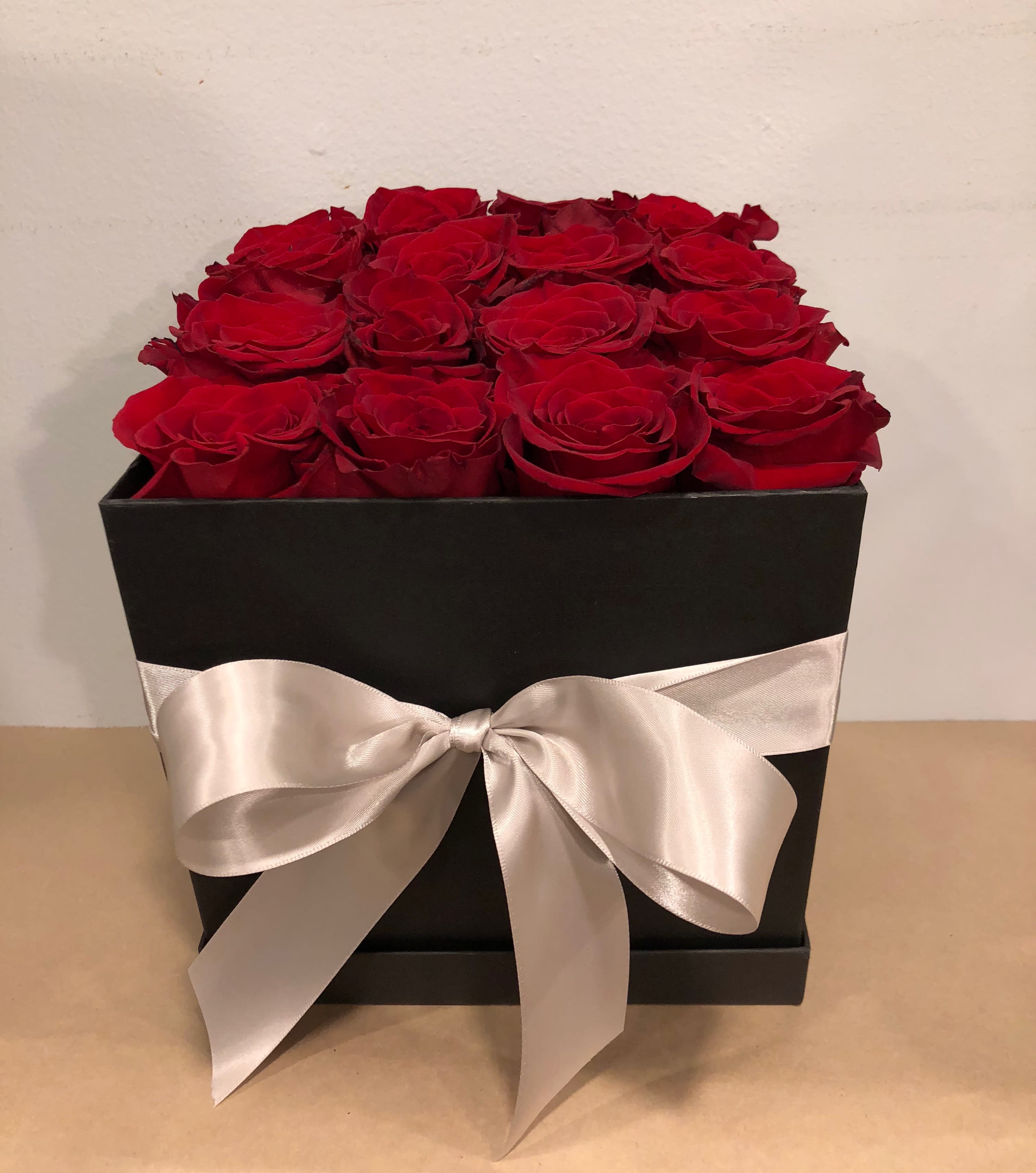 Red roses arranged in a black box with a white satin bow