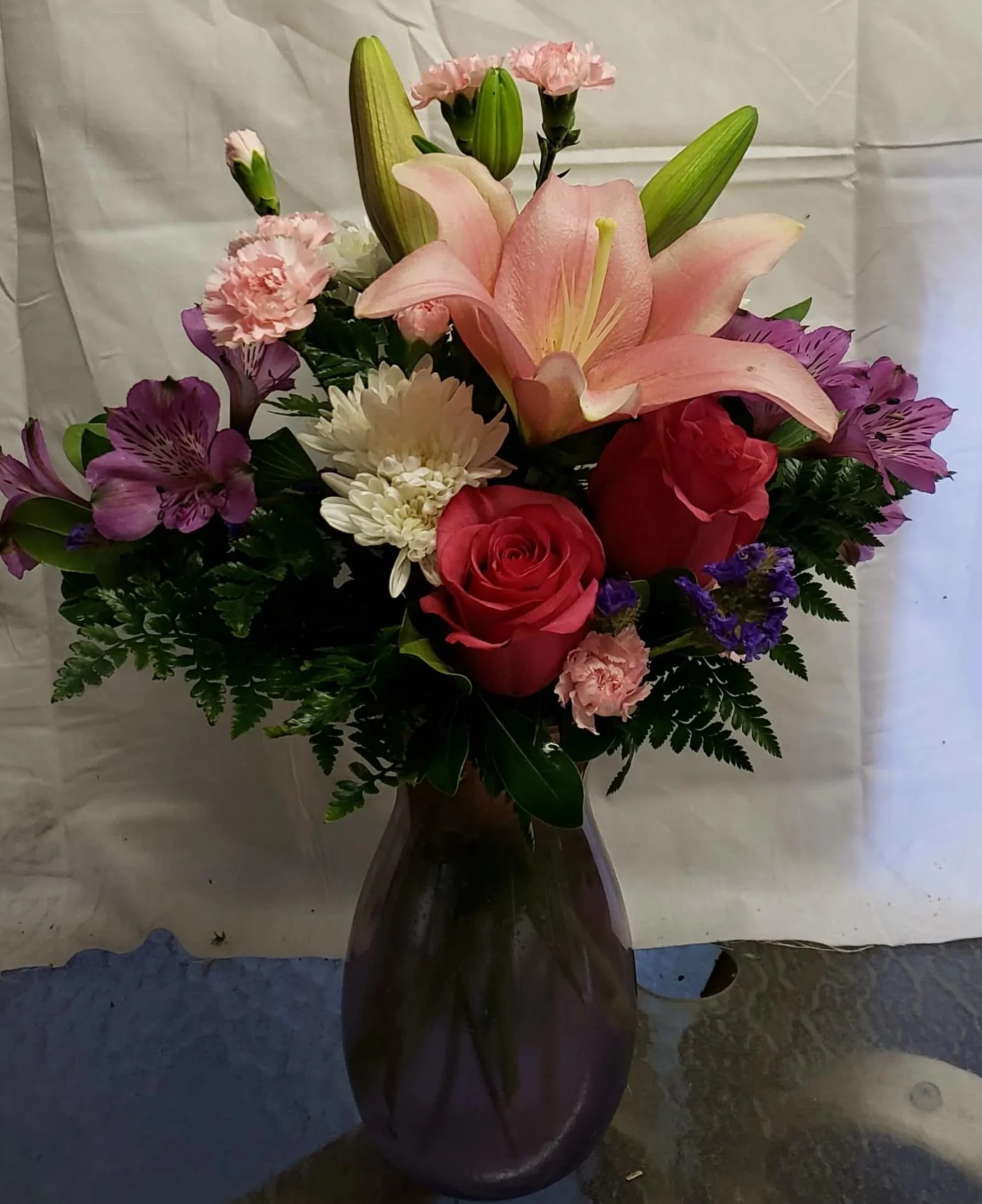 Bouquet of lilies, roses, and purple alstroemeria in a dark vase