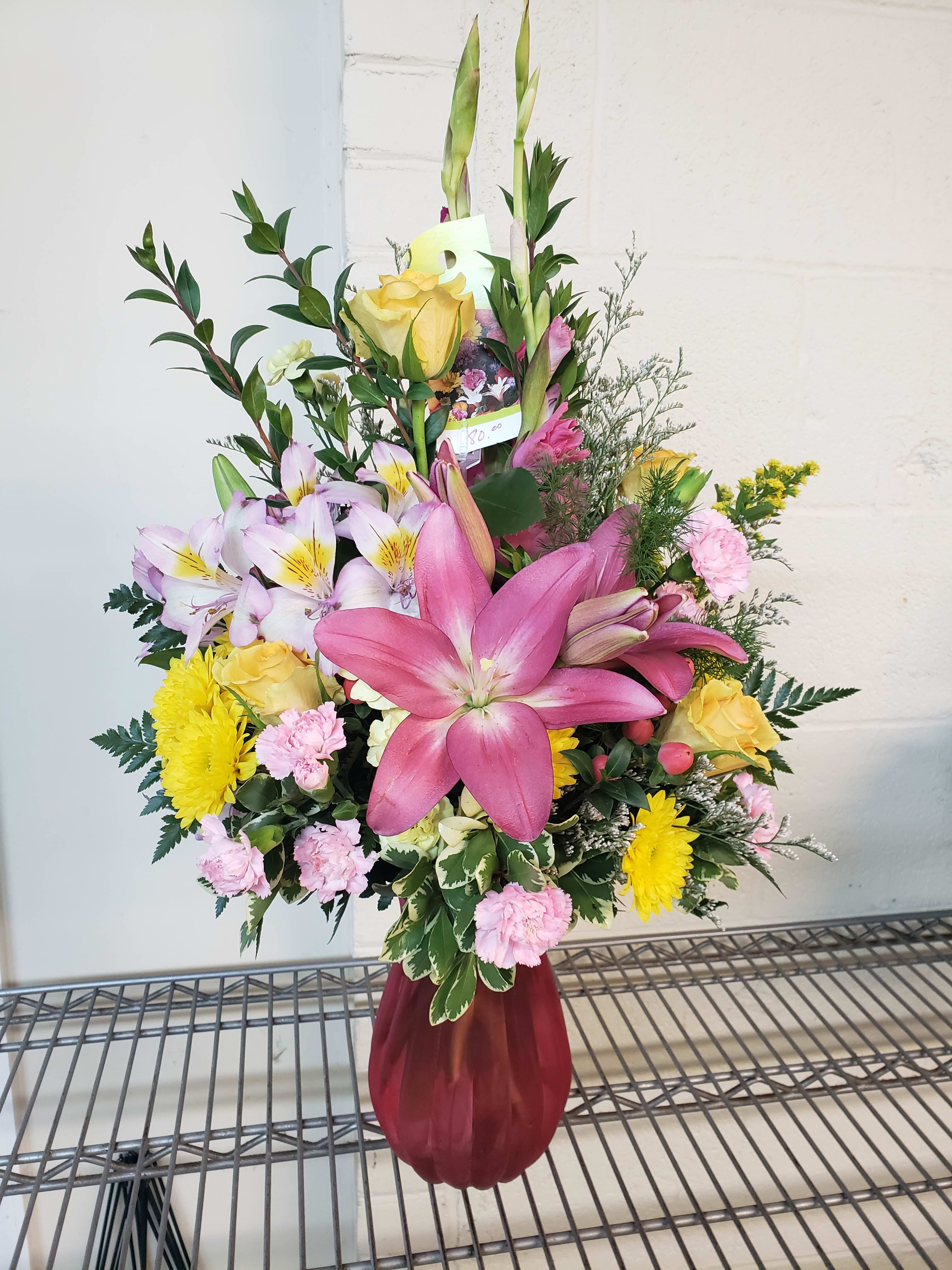 Mixed bouquet with pink lilies, yellow roses, and pink carnations in a burgundy vase