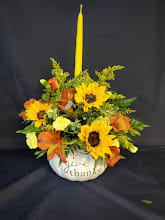 Sunflower and orange floral arrangement in a white vase with a tall yellow candle