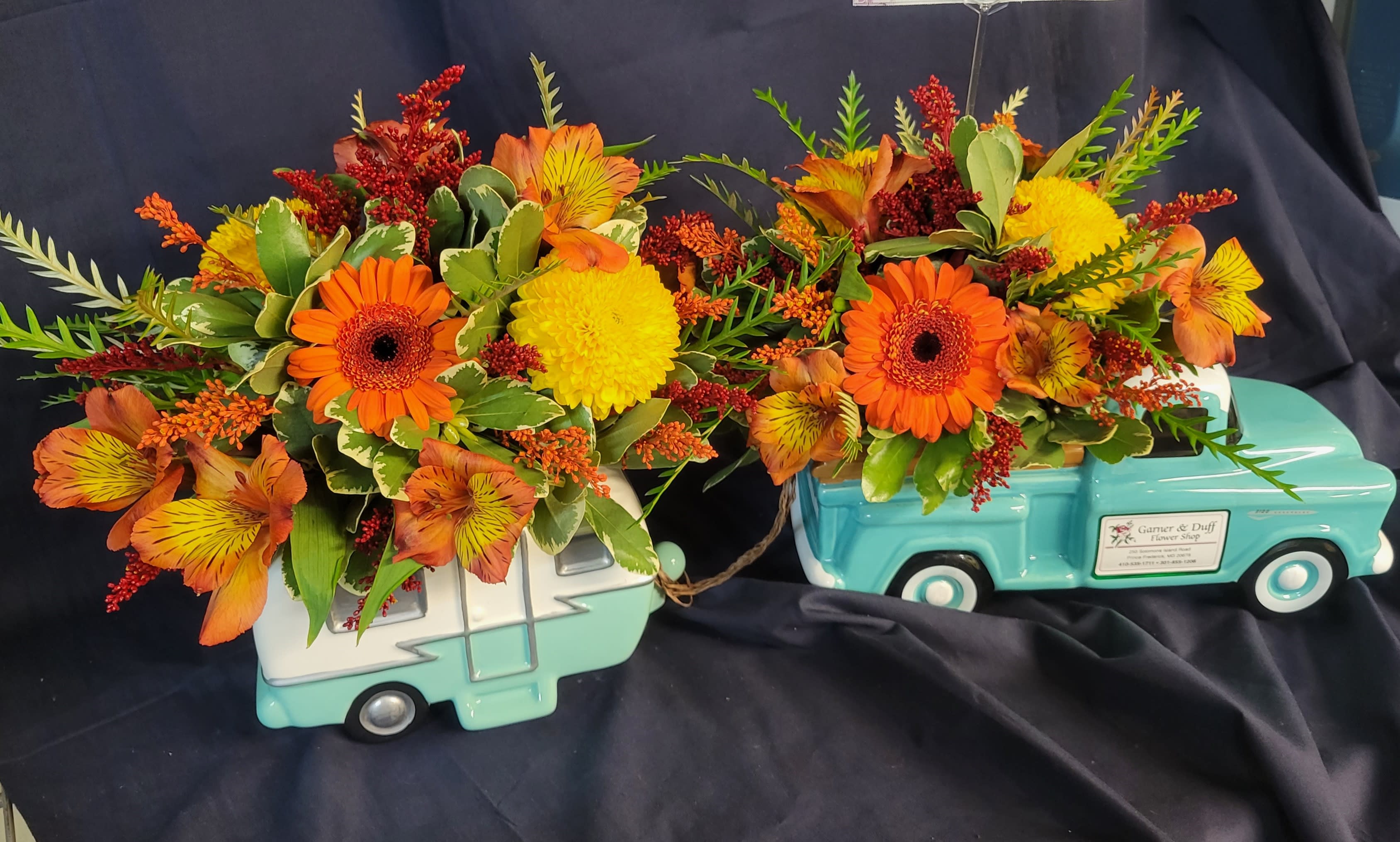 Two floral arrangements in turquoise truck containers with orange and yellow blooms