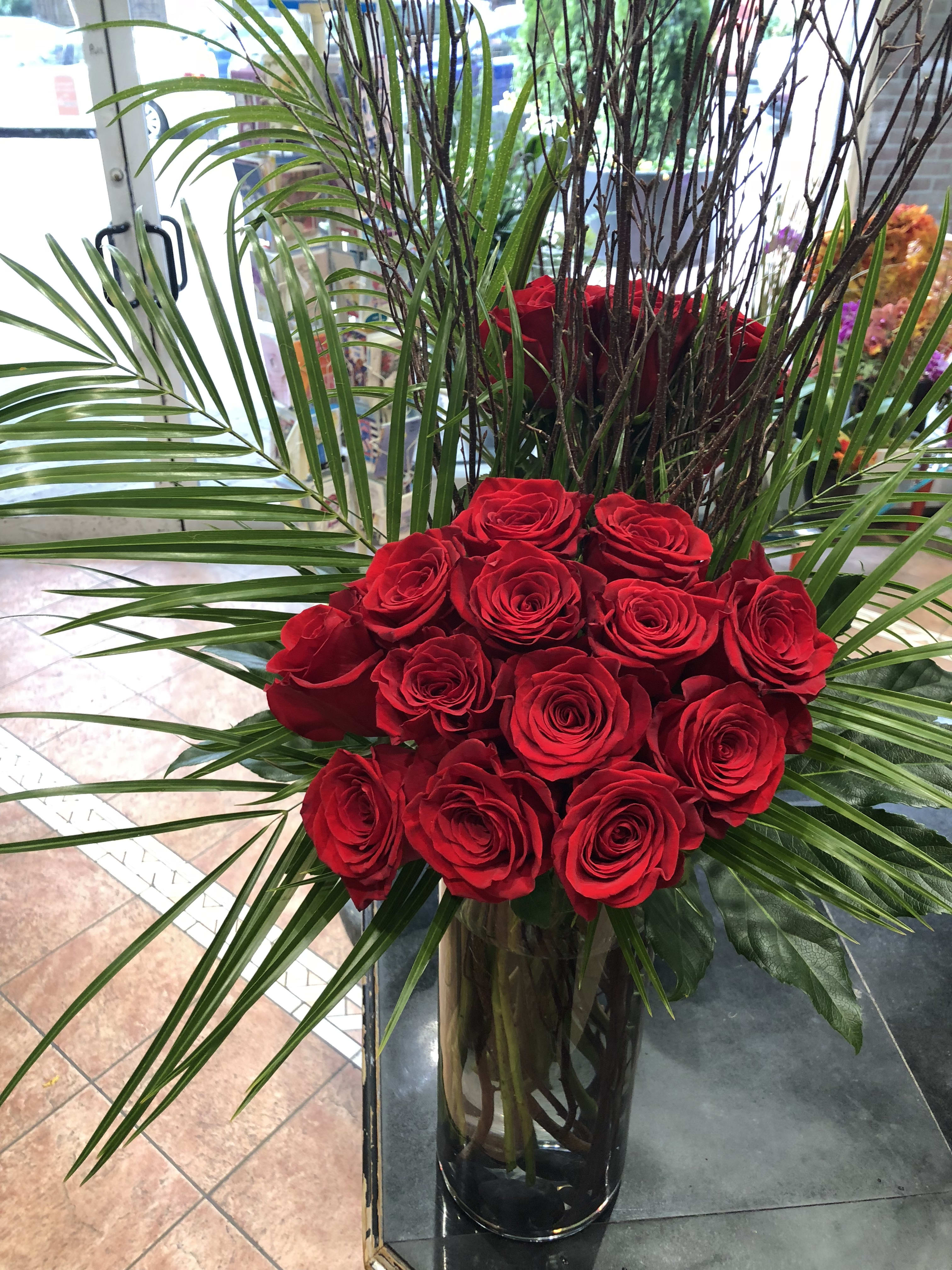 Red roses arranged in a tall glass vase with palm fronds