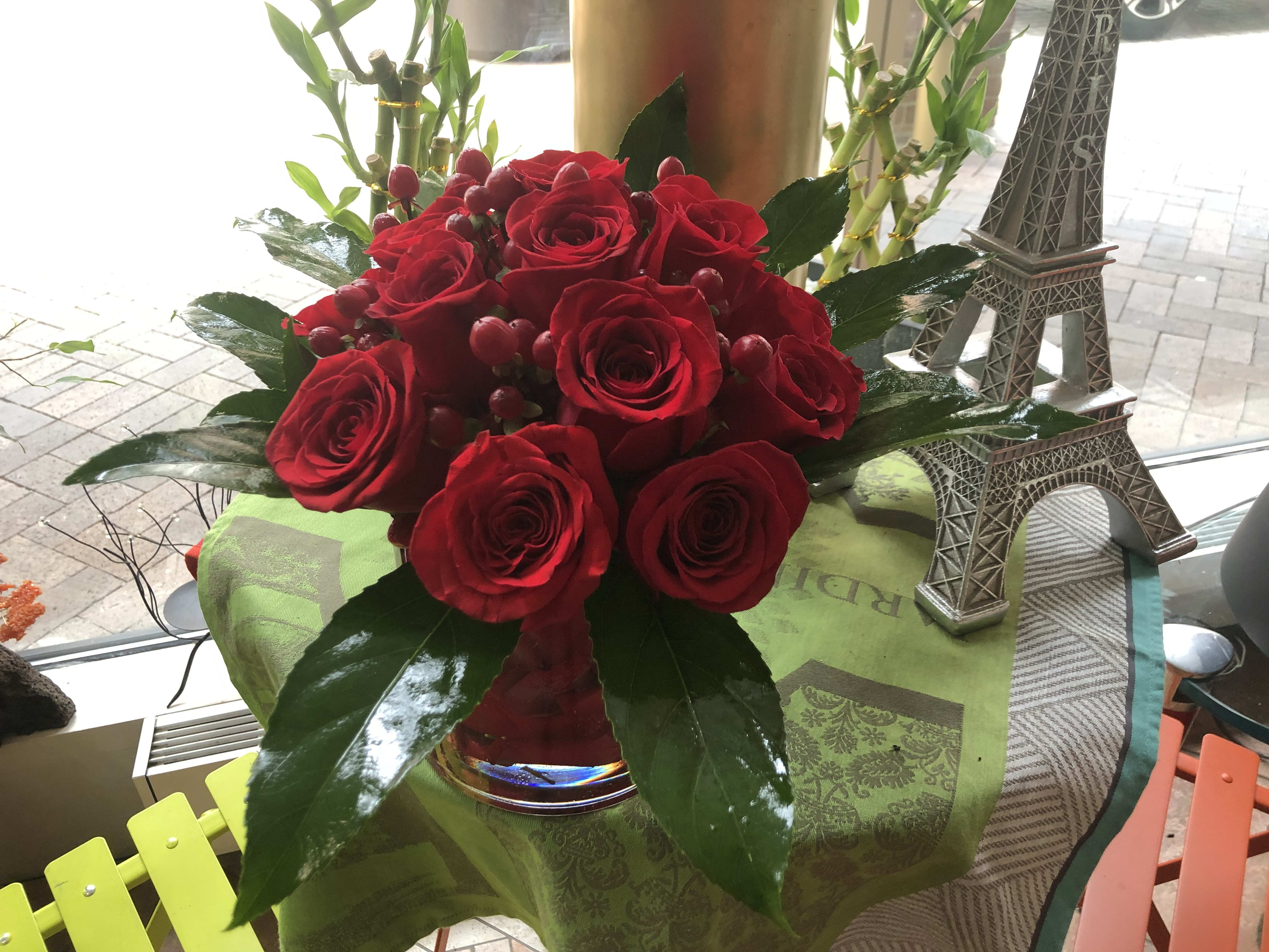 Red roses arranged in a glass vase with glossy leaves