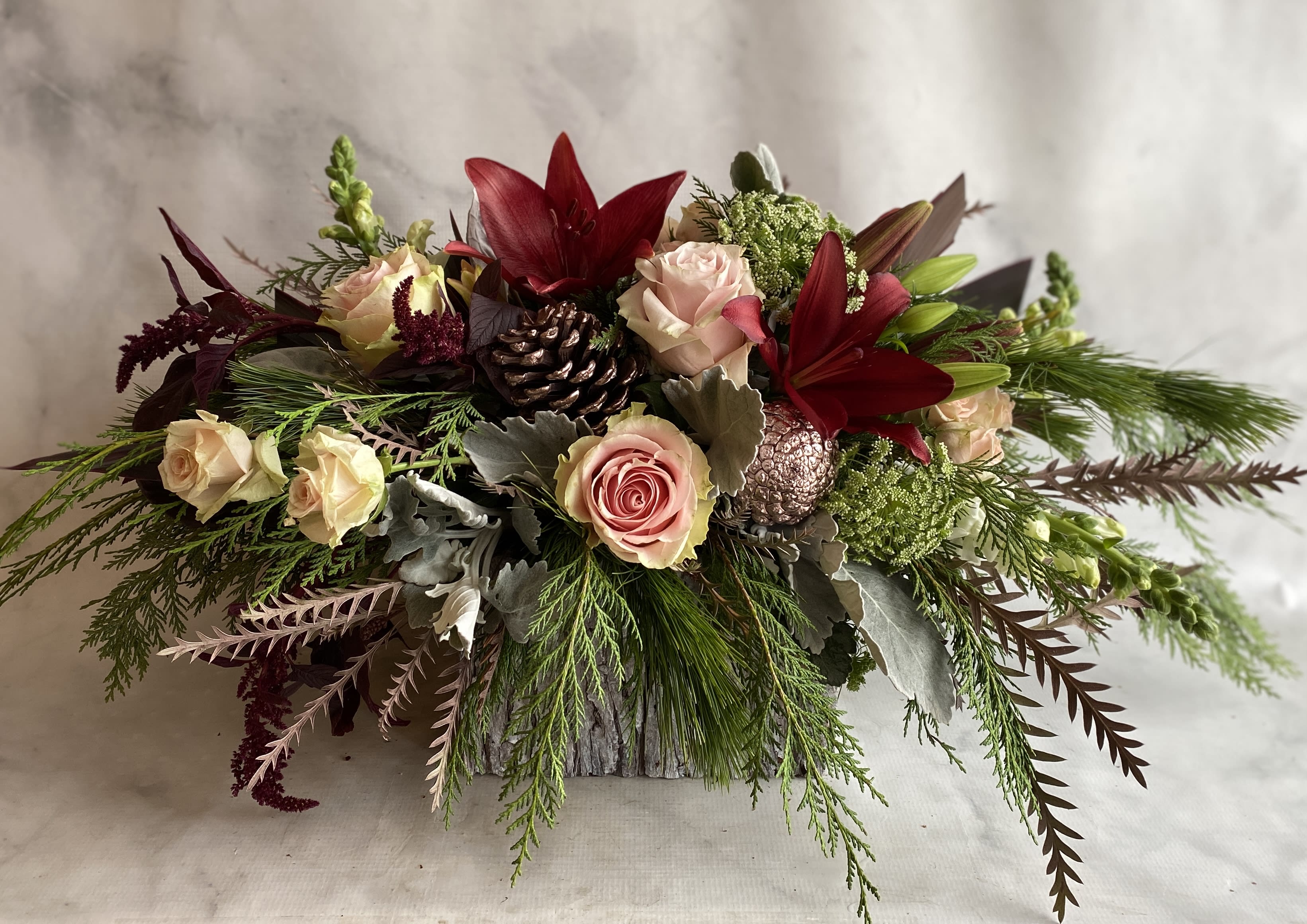 Deck the Halls - Roses, snap dragons, red lilies, pine cones, Xmas greenery and hanging amaranthus fill a bark wood box.