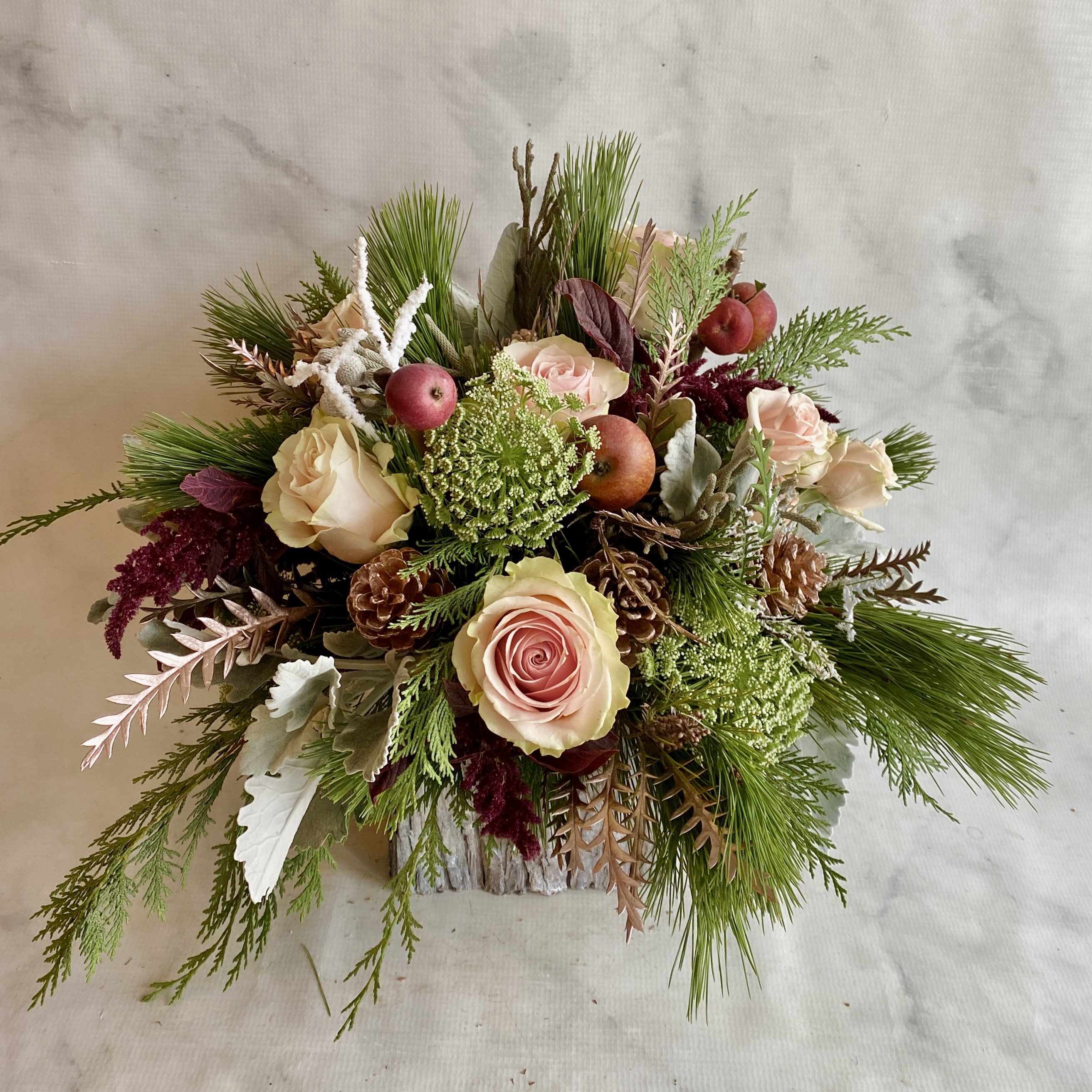 Mixed bouquet of pale roses, pine, and berries in a rustic container
